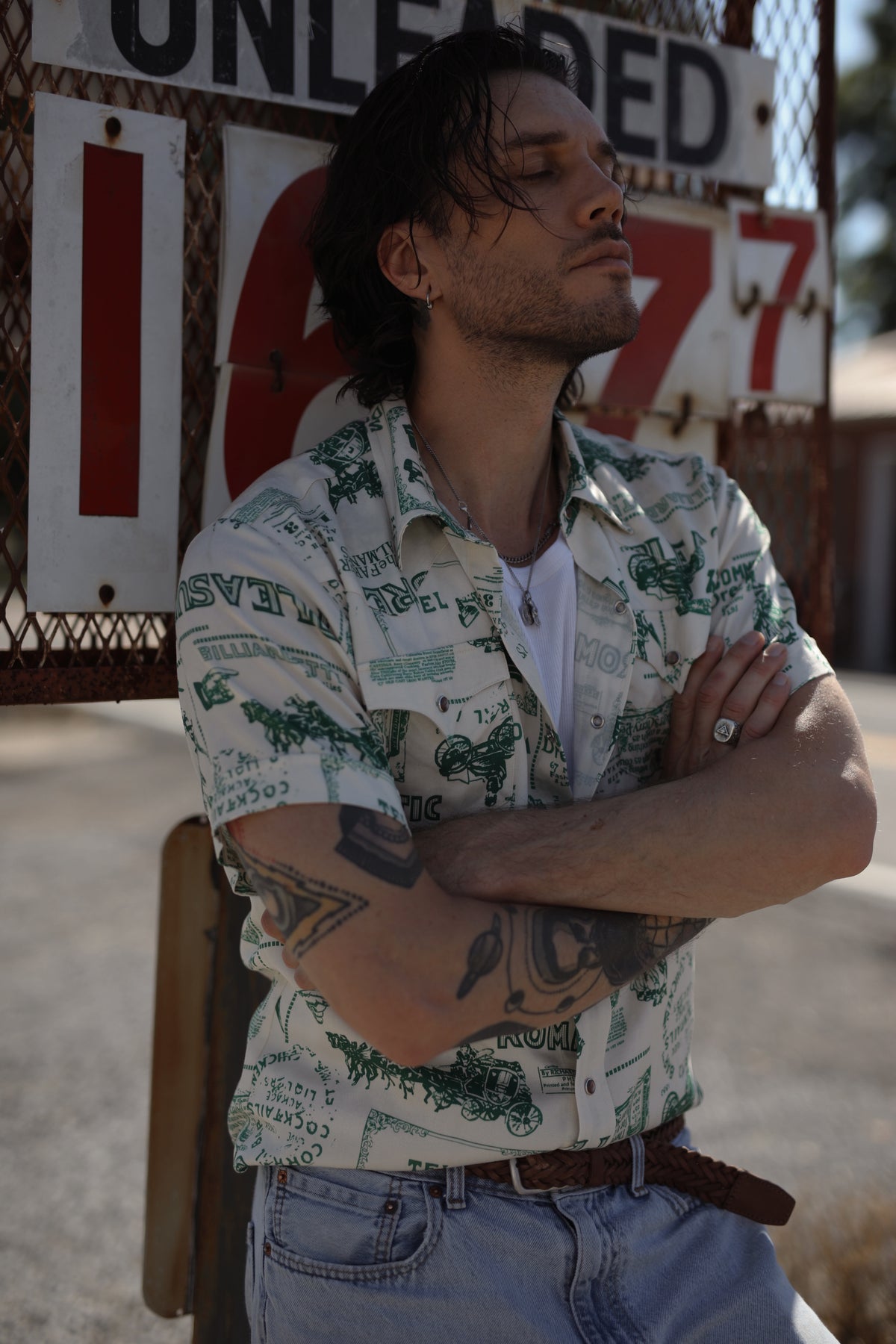 Man with arms crossed outside a retro gas station in the H Bar C Newport Somerville print shirt.