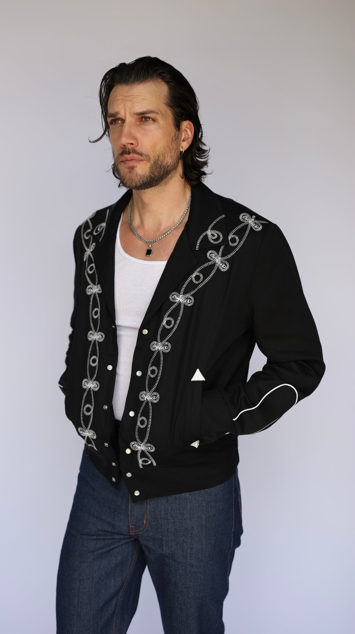 Man in the H Bar C Bolero El Patrón black jacket with white embroidery over a white tee and jeans.