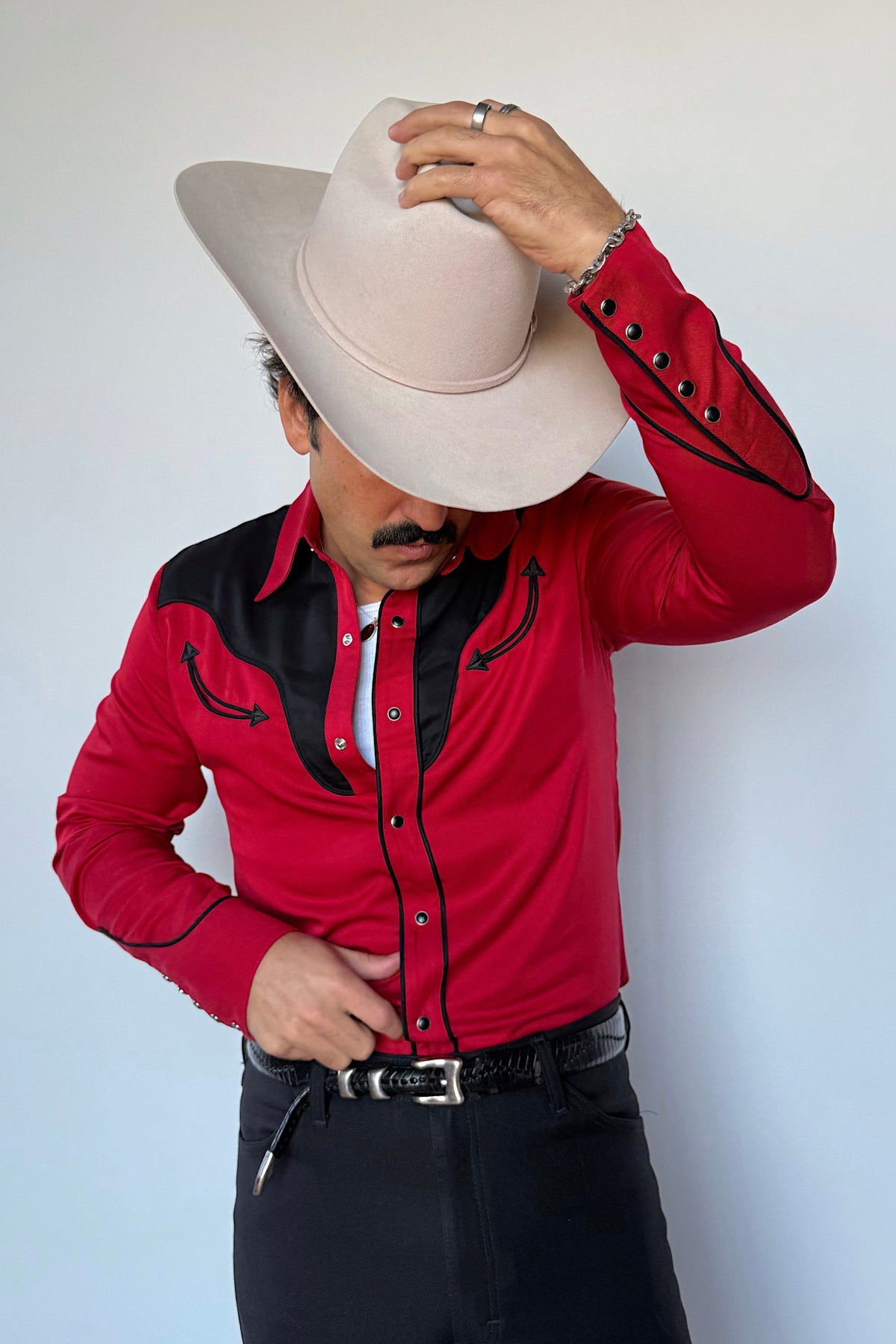 Man tipping his cowboy hat in the H Bar C San Juan red and black two-tone western shirt with black pants.