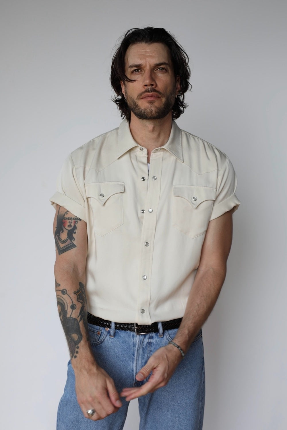 Man wearing the H Bar C Newport short sleeve western shirt in off white with pearl snaps and pointed pockets, tucked into jeans.