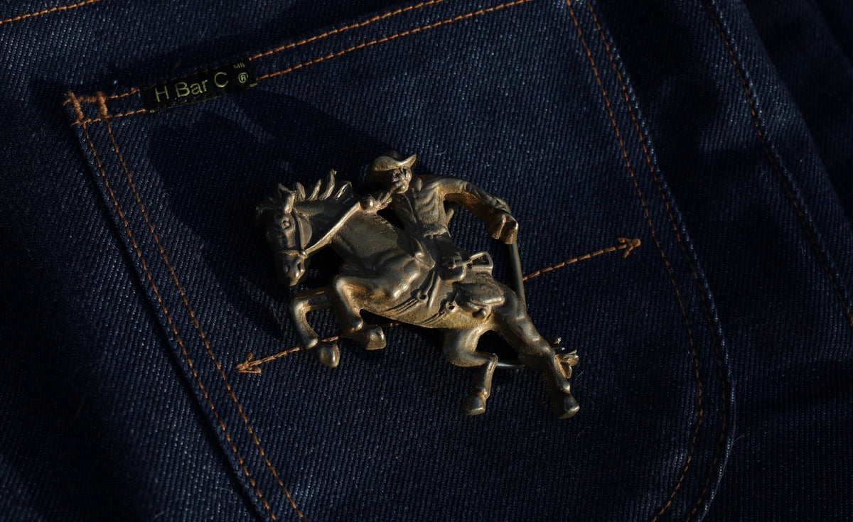 H Bar C Five Pieces of the Frontier gold bucking horse belt buckle on indigo denim.