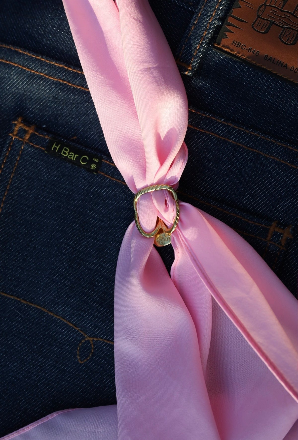 Close-up of the H Bar C cowboy hat scarf slide holding a pink silk wild rag.