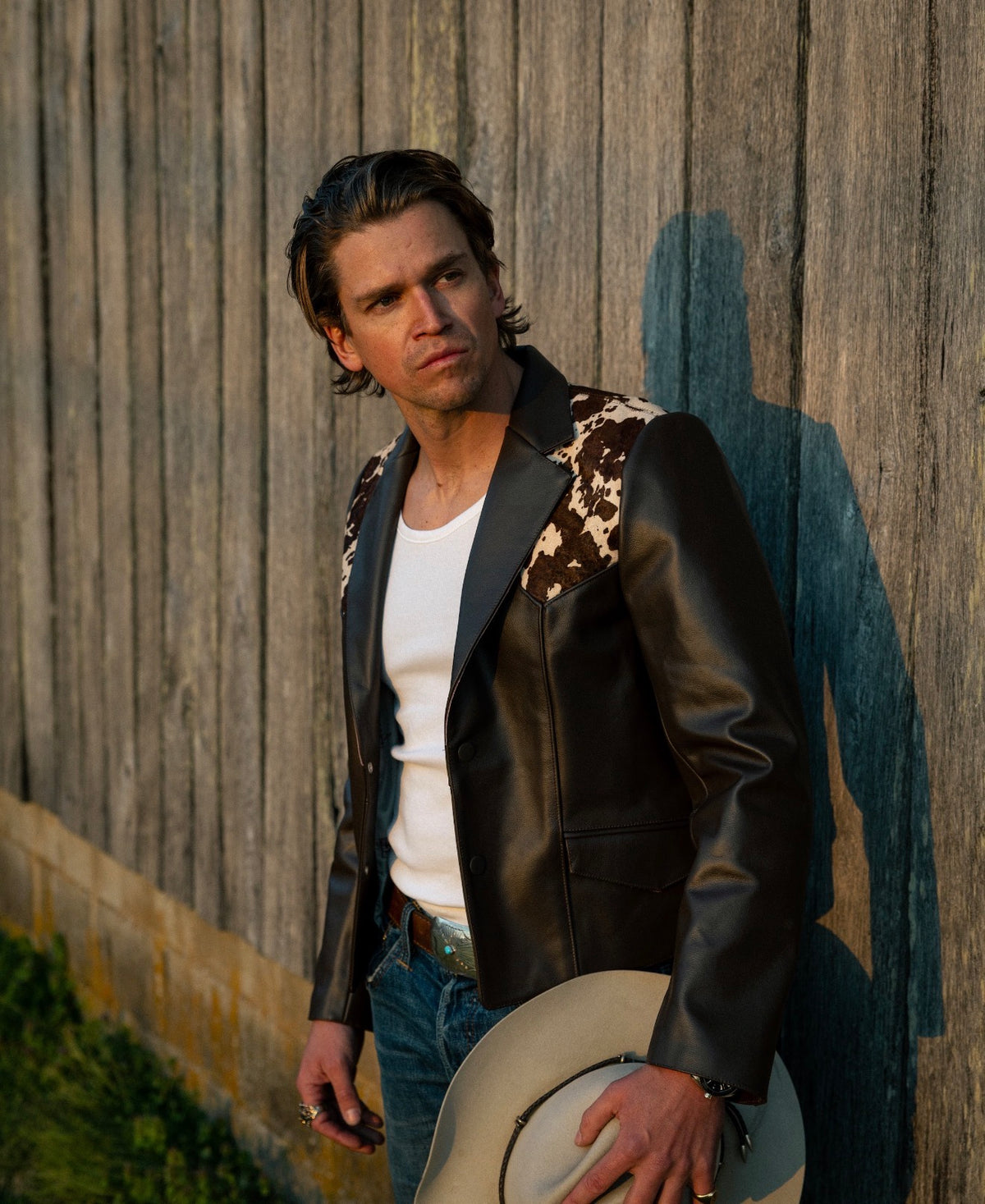 Man by a weathered barn wearing the H Bar C Cody brown leather and cowhide jacket.