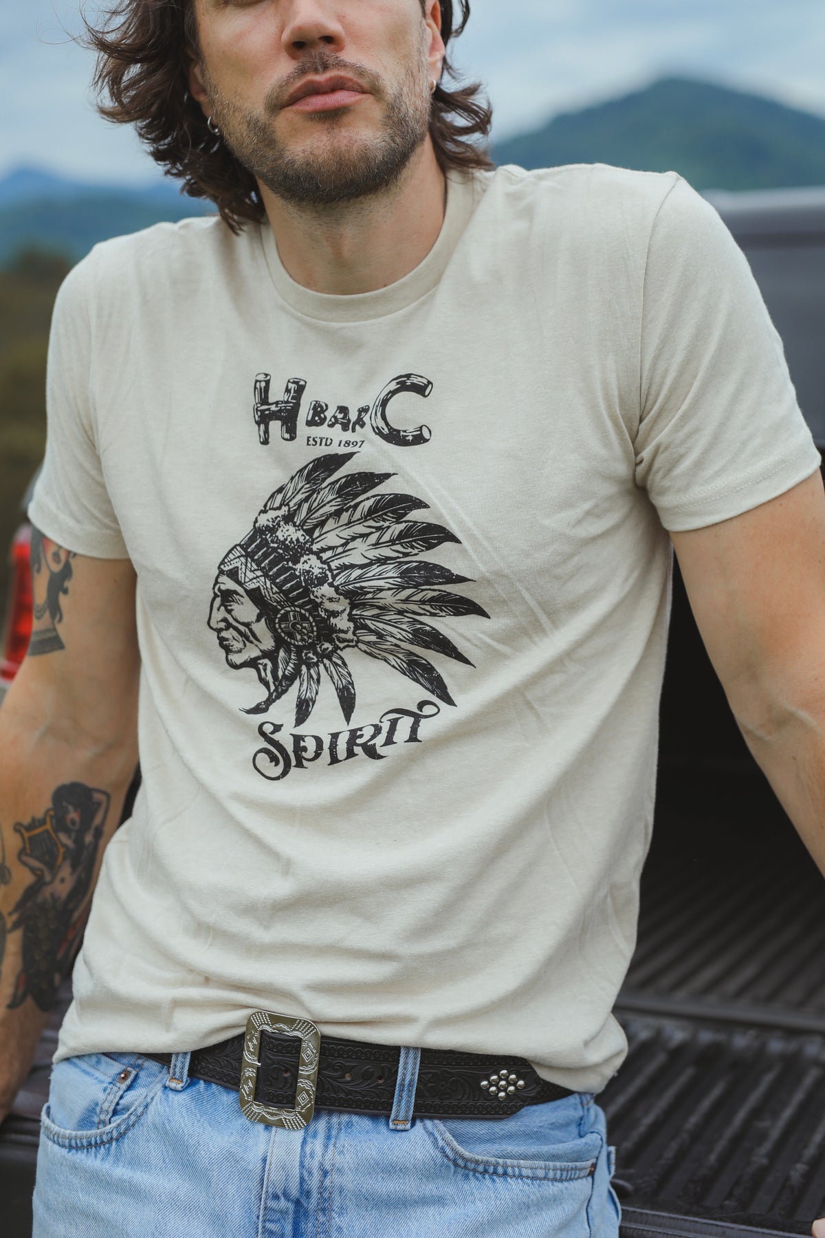 Man wearing the H Bar C Sand Spirit T-shirt in cream with a vintage chief graphic and H Bar C Spirit lettering.
