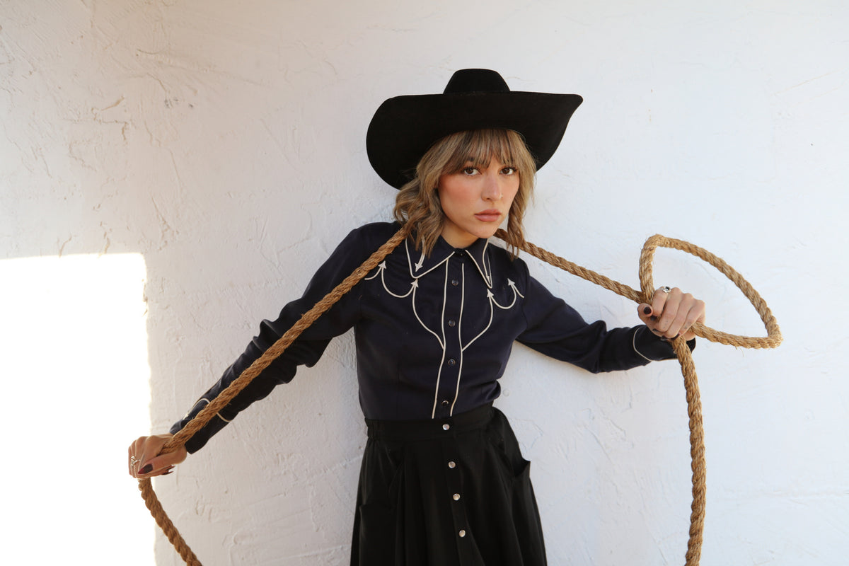 Woman swinging a rope lariat in the H Bar C Lake Tahoe navy western shirt with white piping.