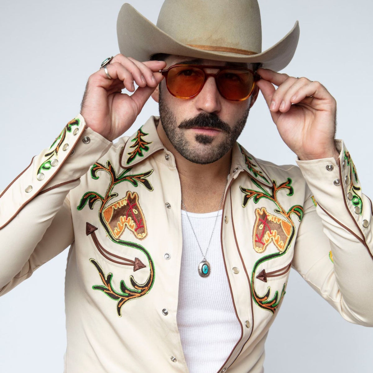 Man adjusting his cowboy hat wearing the H Bar C Calabasas off-white chain stitch western shirt.