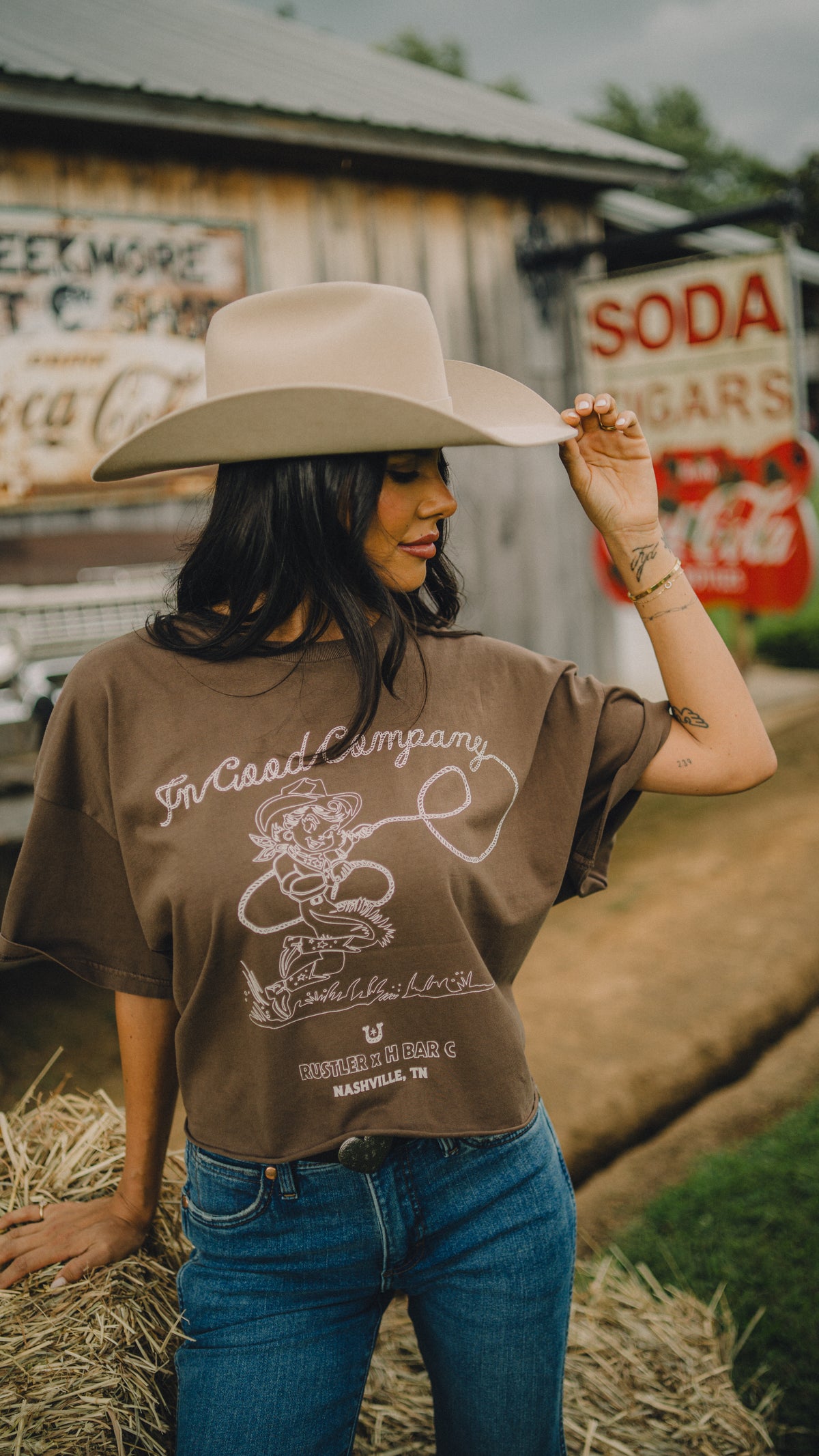 Woman tipping her hat in the H Bar C x Rustler In Good Company brown crop tee with cowgirl graphic.