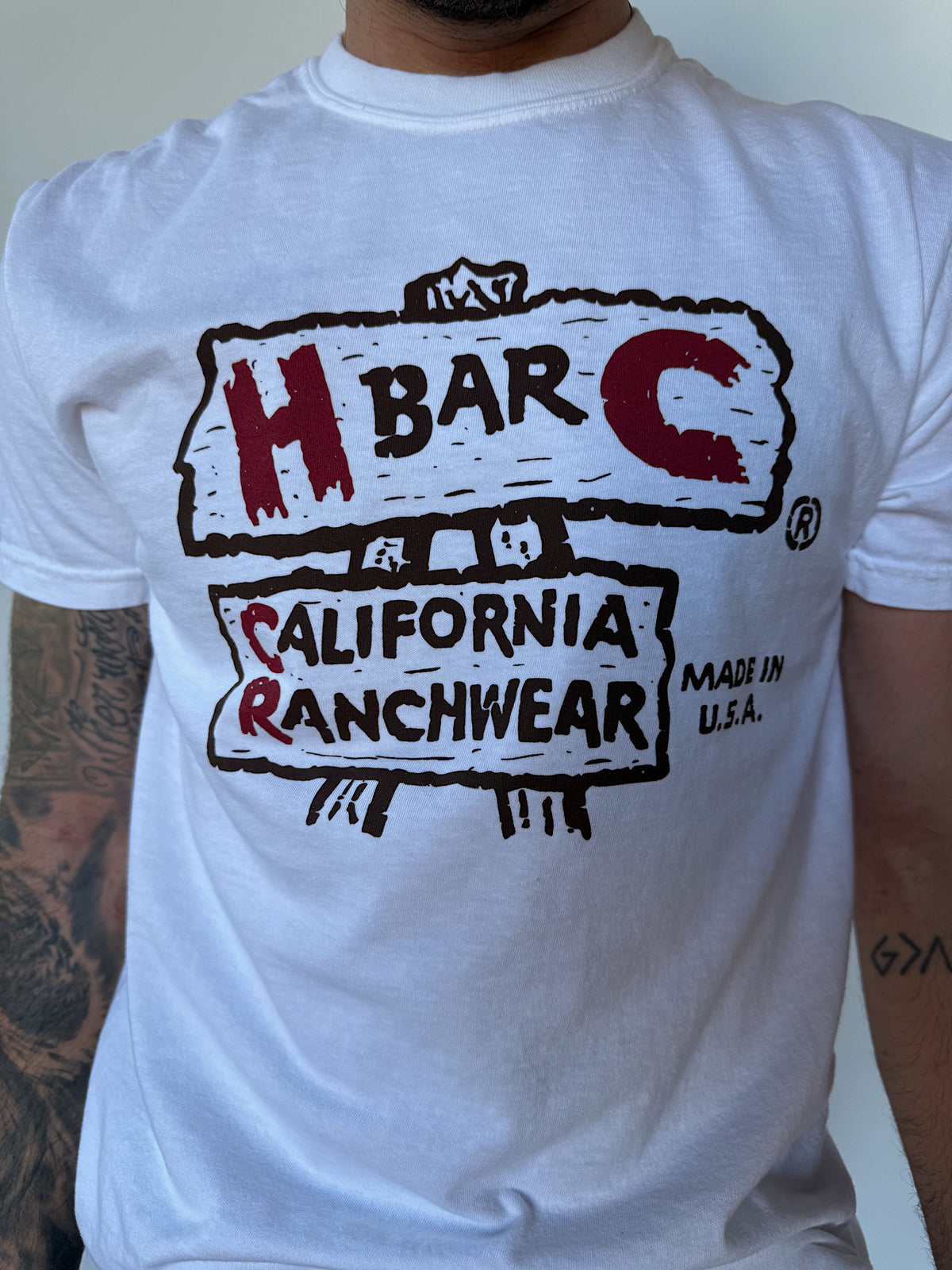 Close-up of the red and black H Bar C California Ranchwear vintage logo on the white Rattlesnake Junction T-shirt.