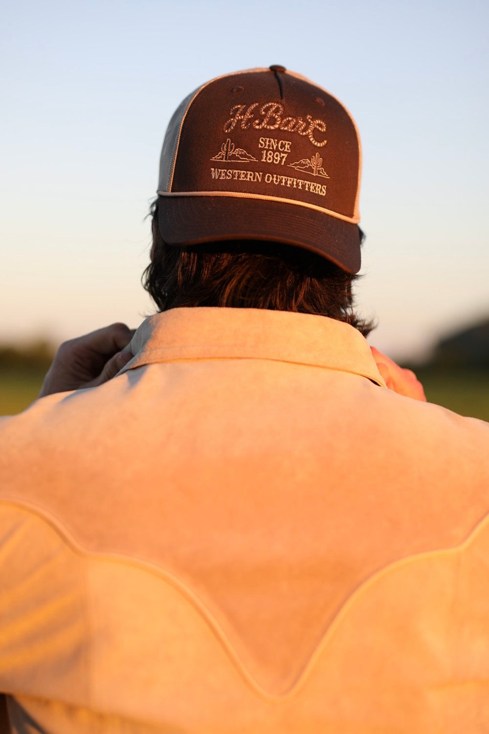 Brown H Bar C rope baseball hat worn at sunset with a western jacket.