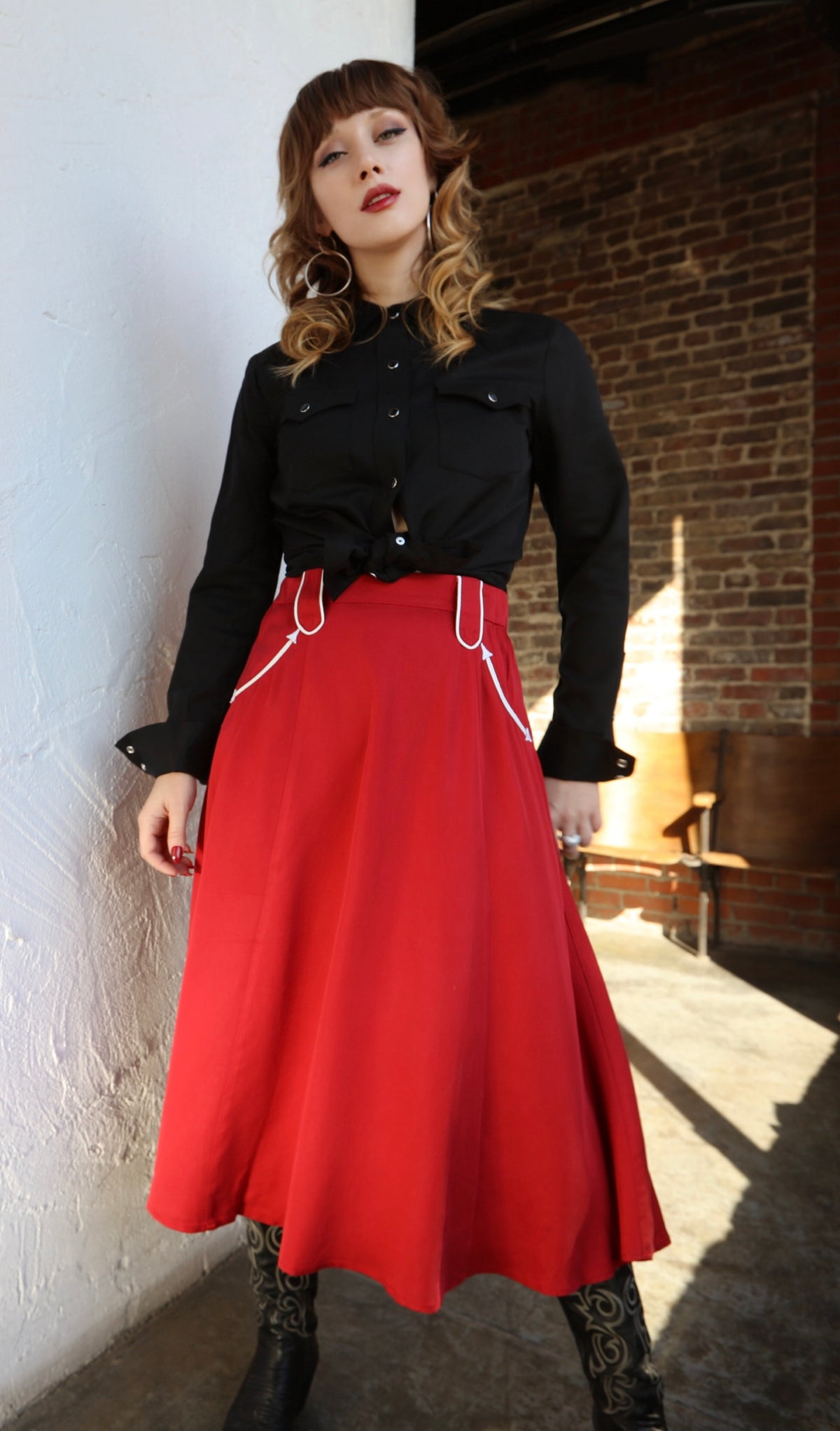 Woman wearing the H Bar C Santa Fe red swing skirt with a black western shirt in a sunlit room.