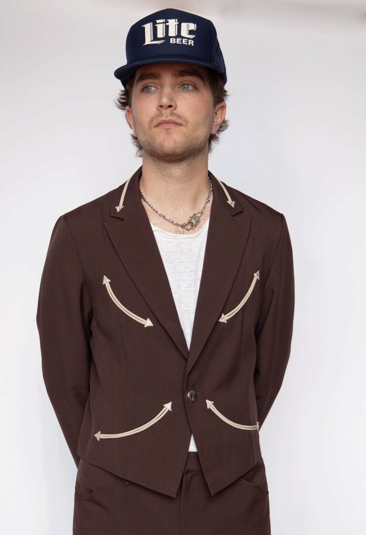 Man in a trucker cap wearing the H Bar C Calamity chocolate jacket over a white tee.