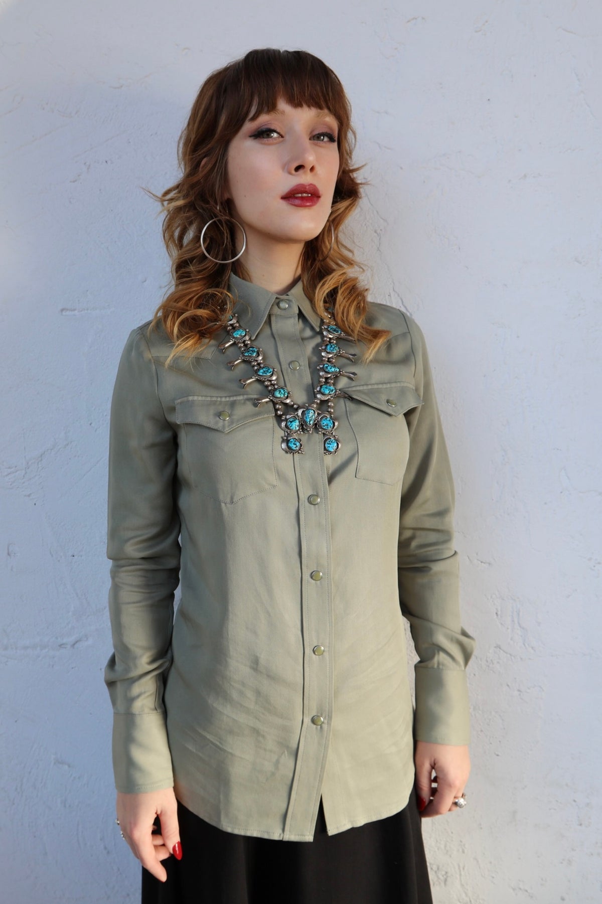 Woman wearing the H Bar C Denver women's shirt in sage green with a turquoise necklace, our classic pearl snap western shirt.