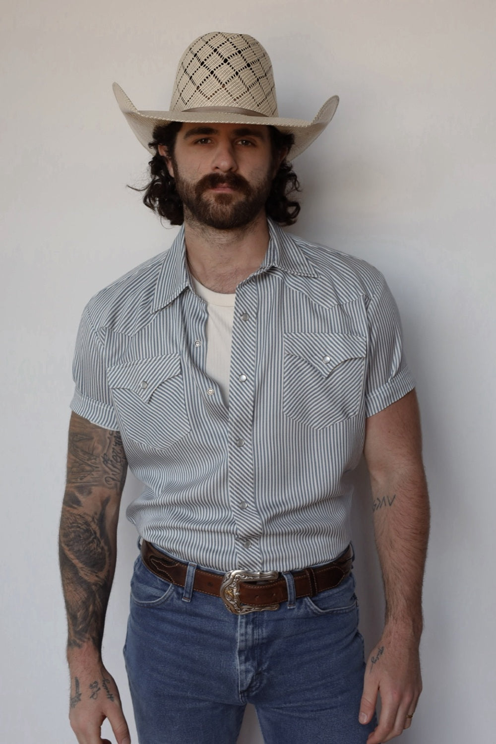 Man in a straw cowboy hat wearing the H Bar C Newport short sleeve western shirt in gray stripe with pearl snaps and jeans.