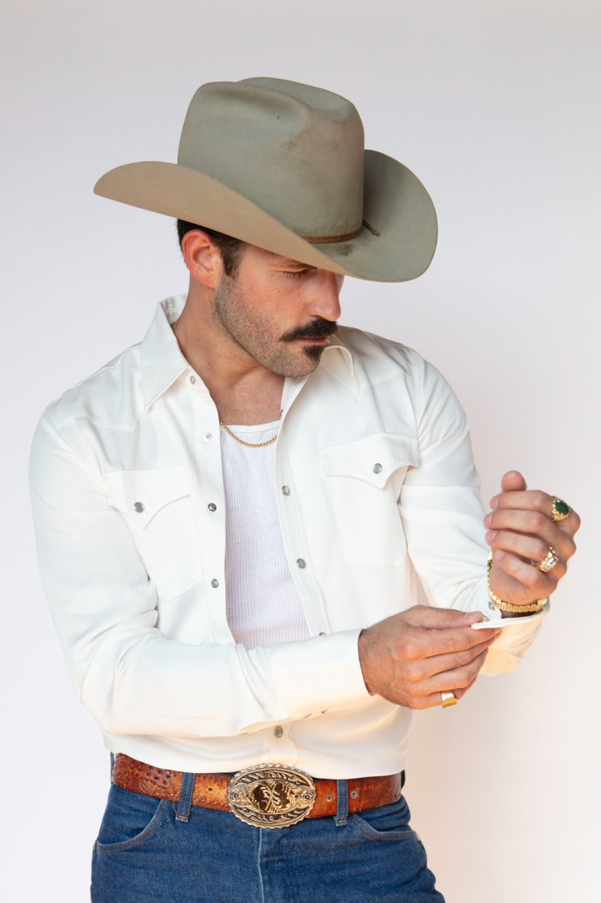 Man in a cowboy hat fastening the cuff of the H Bar C Denver men's shirt in white, a Tencel pearl snap western shirt made since 1938.