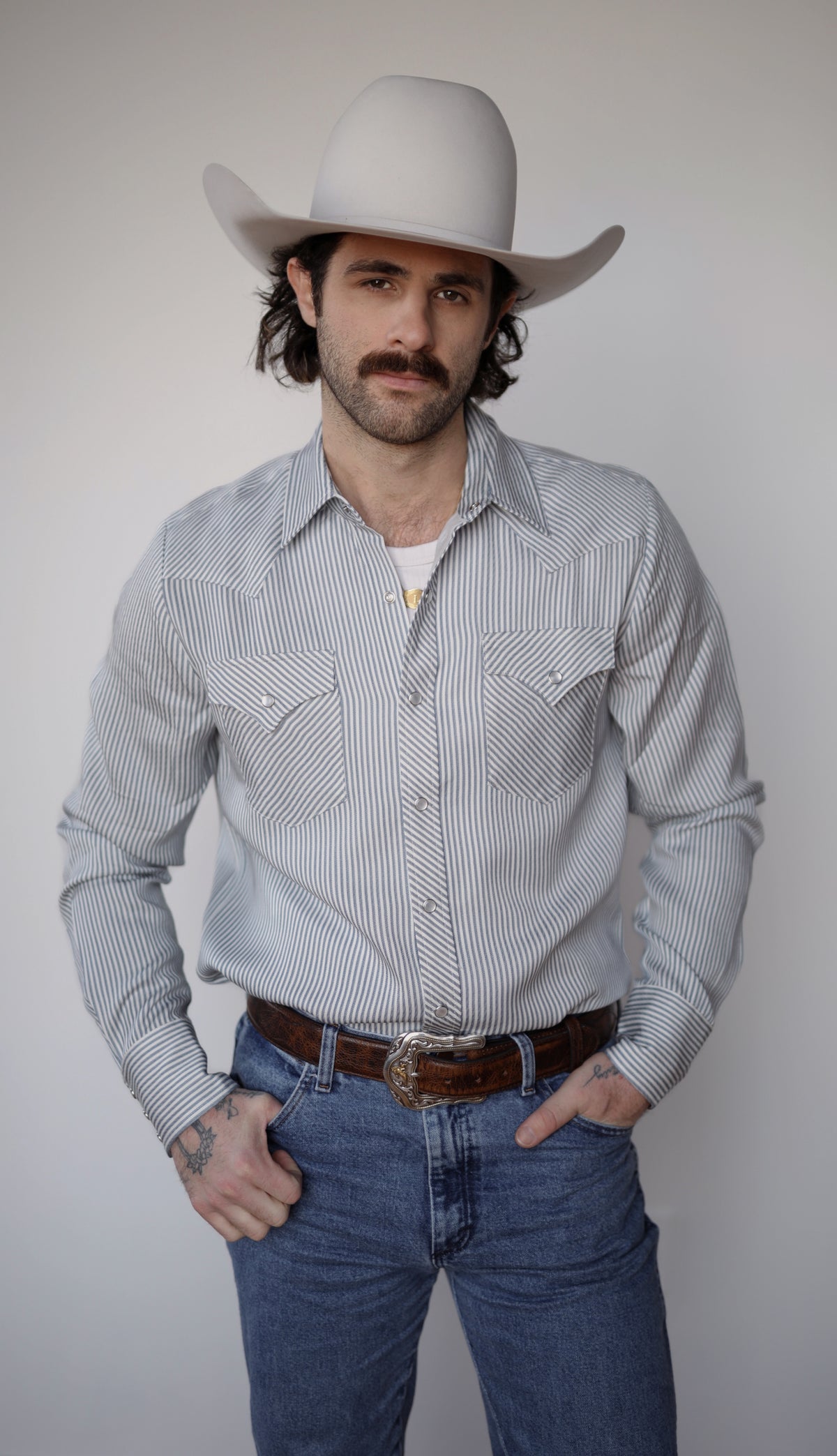 Man in a cowboy hat wearing the H Bar C Folsom blue pinstripe western shirt with hands in pockets.