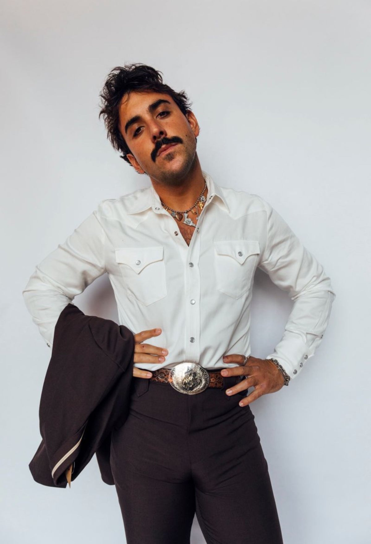Man wearing the H Bar C Denver white pearl snap shirt with dark pants and silver buckle, holding a jacket over his arm.