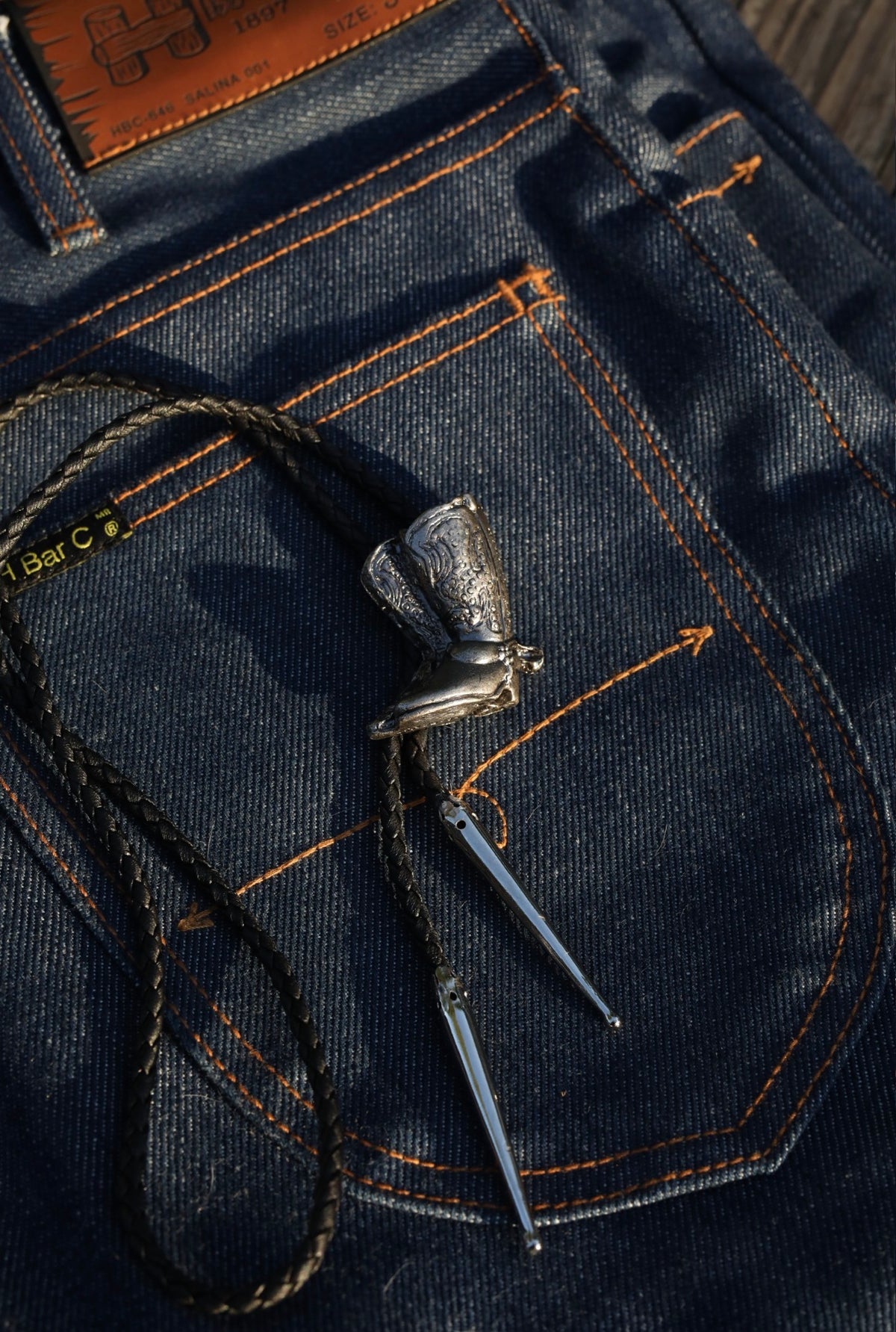 Detail of the engraved silver cowboy boot slide on the H Bar C bolo tie.