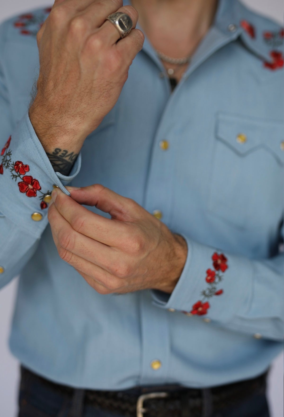 Man adjusting the embroidered cuff of the HBarC x Gibson Dove chambray western shirt with red poppy details.