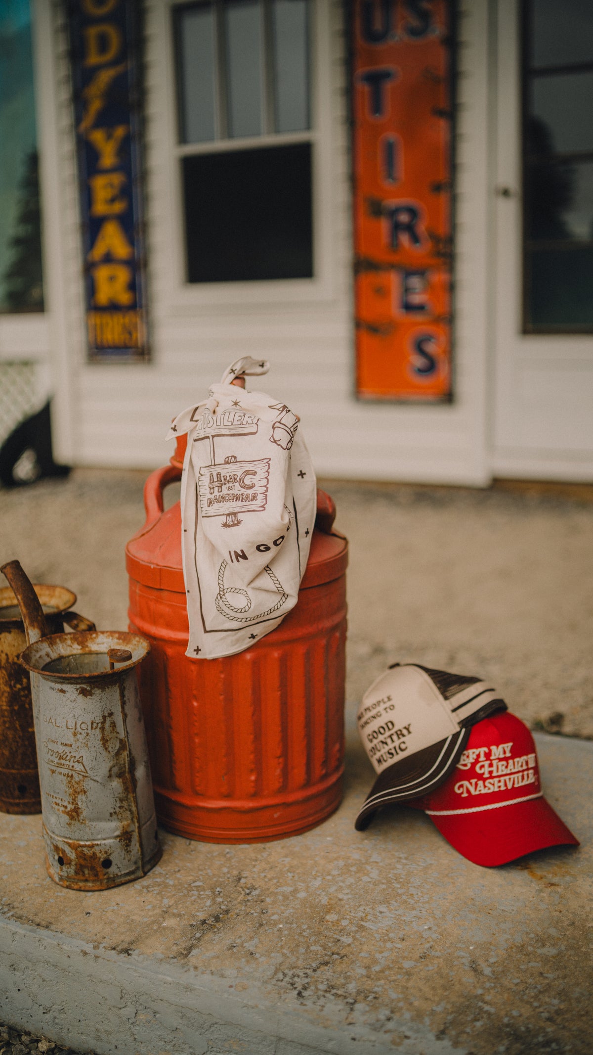 H Bar C x Rustler cream bandana on a red oil can outside a vintage gas station.