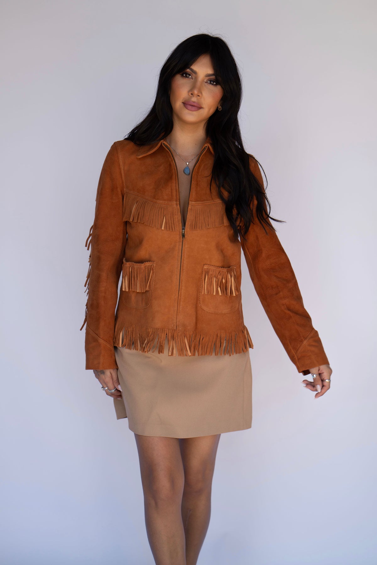 Full length view of the H Bar C Omaha brown suede buckskin fringe jacket over a beige skirt.