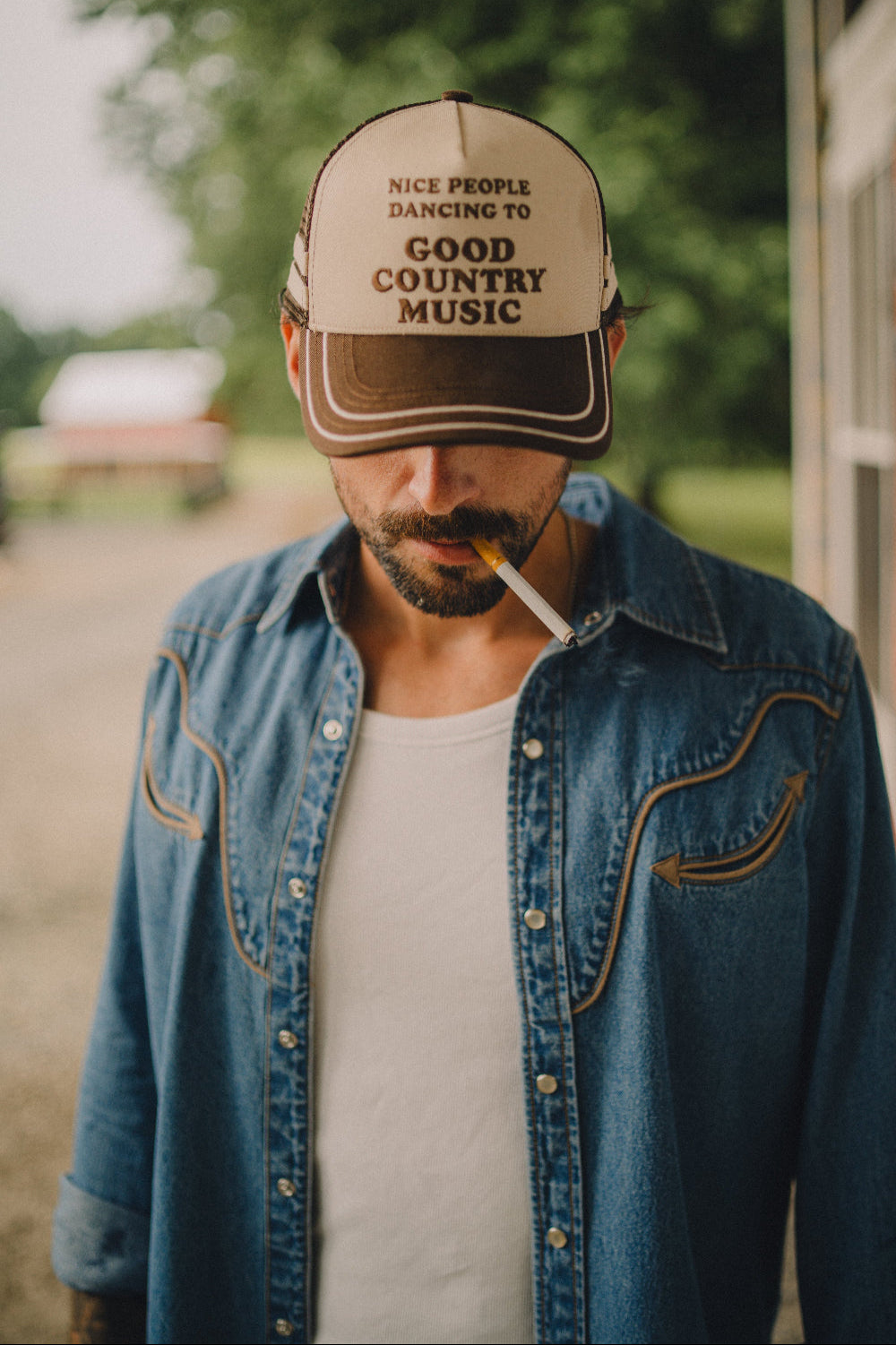 Man wearing the H Bar C x Rustler Nice People trucker hat with a denim shirt outdoors.