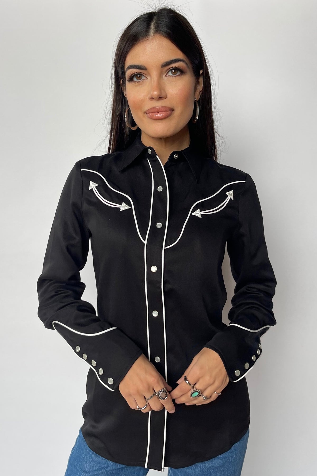 Woman wearing the H Bar C San Fernando women's shirt in black with white piping and arrow details, a 100 year H Bar C classic.