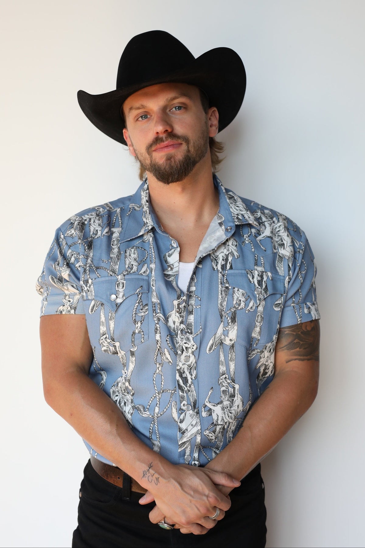 Man in a black cowboy hat wearing the H Bar C Newport Breckenridge short sleeve western shirt in light blue with a cream western print.