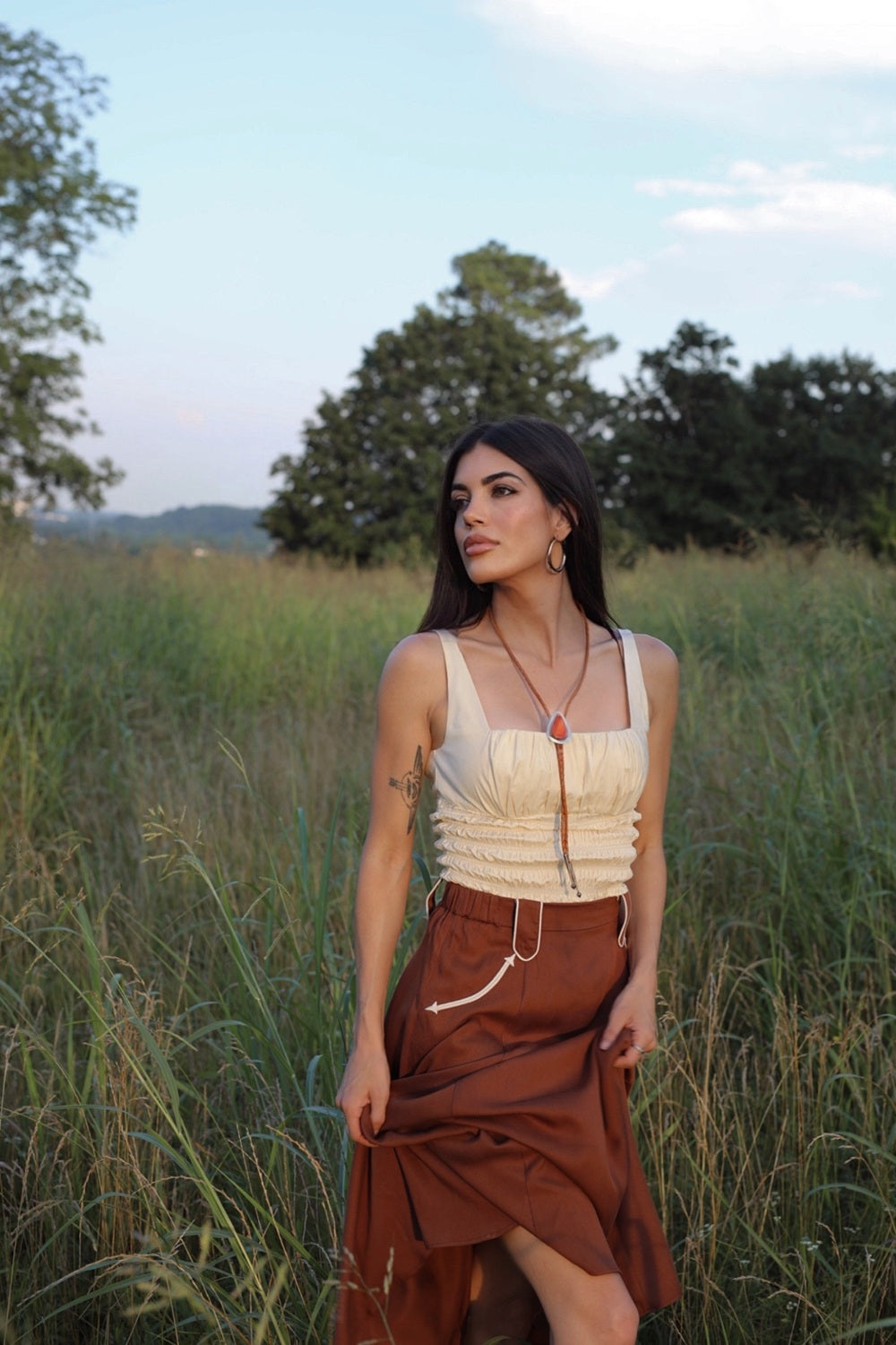 Woman in a grassy field at sunset wearing the H Bar C Santa Fe chocolate skirt with a cream top.