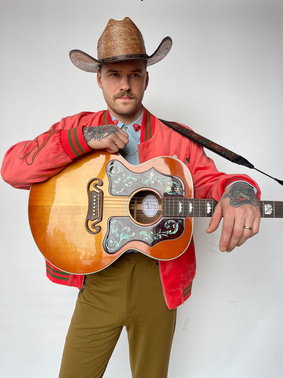 Man in a cowboy hat holding an acoustic guitar, wearing the H Bar C Franklin olive pants with a red western shirt.