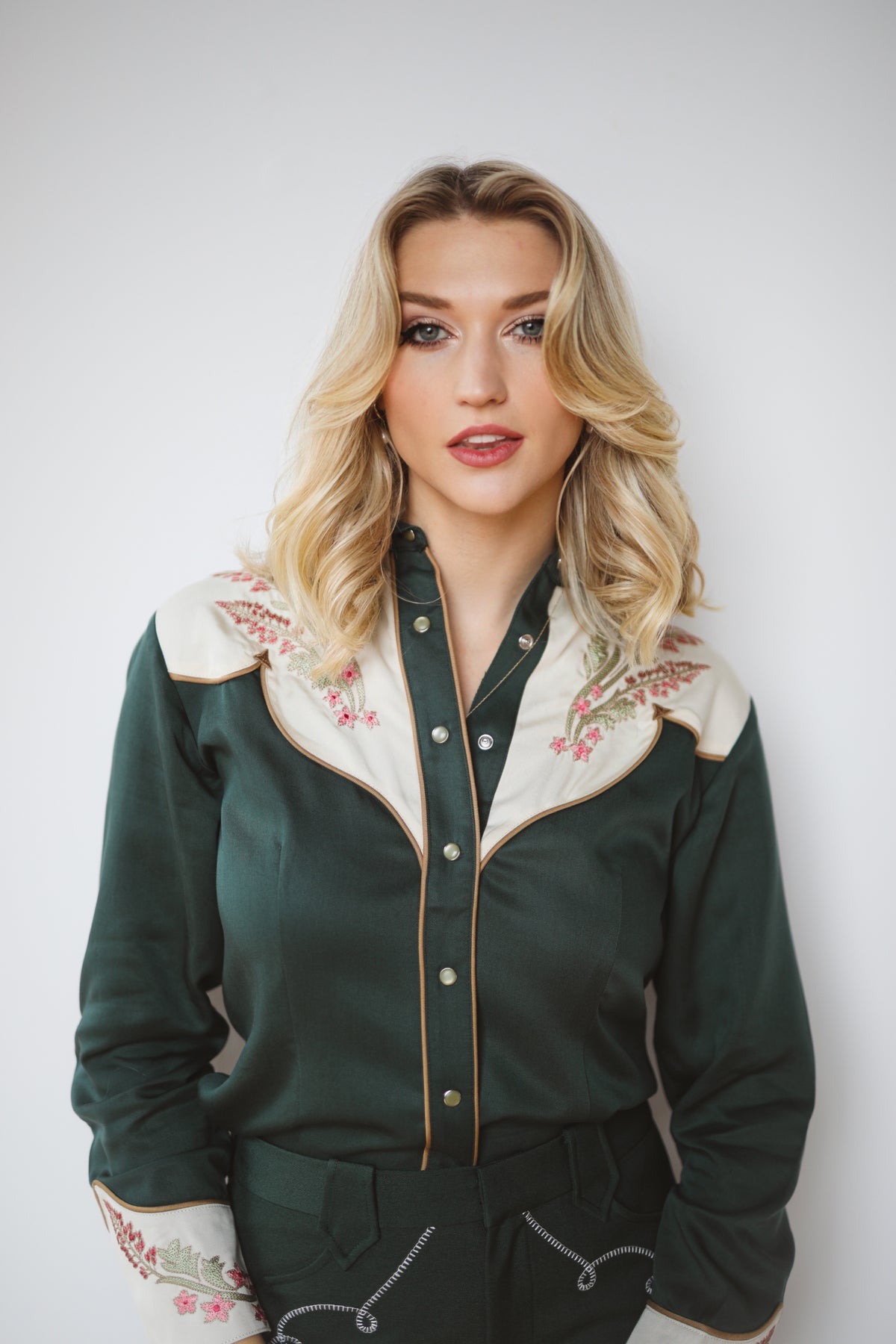 Woman wearing the Tecovas x H Bar C Birthday X green and cream embroidered western shirt.