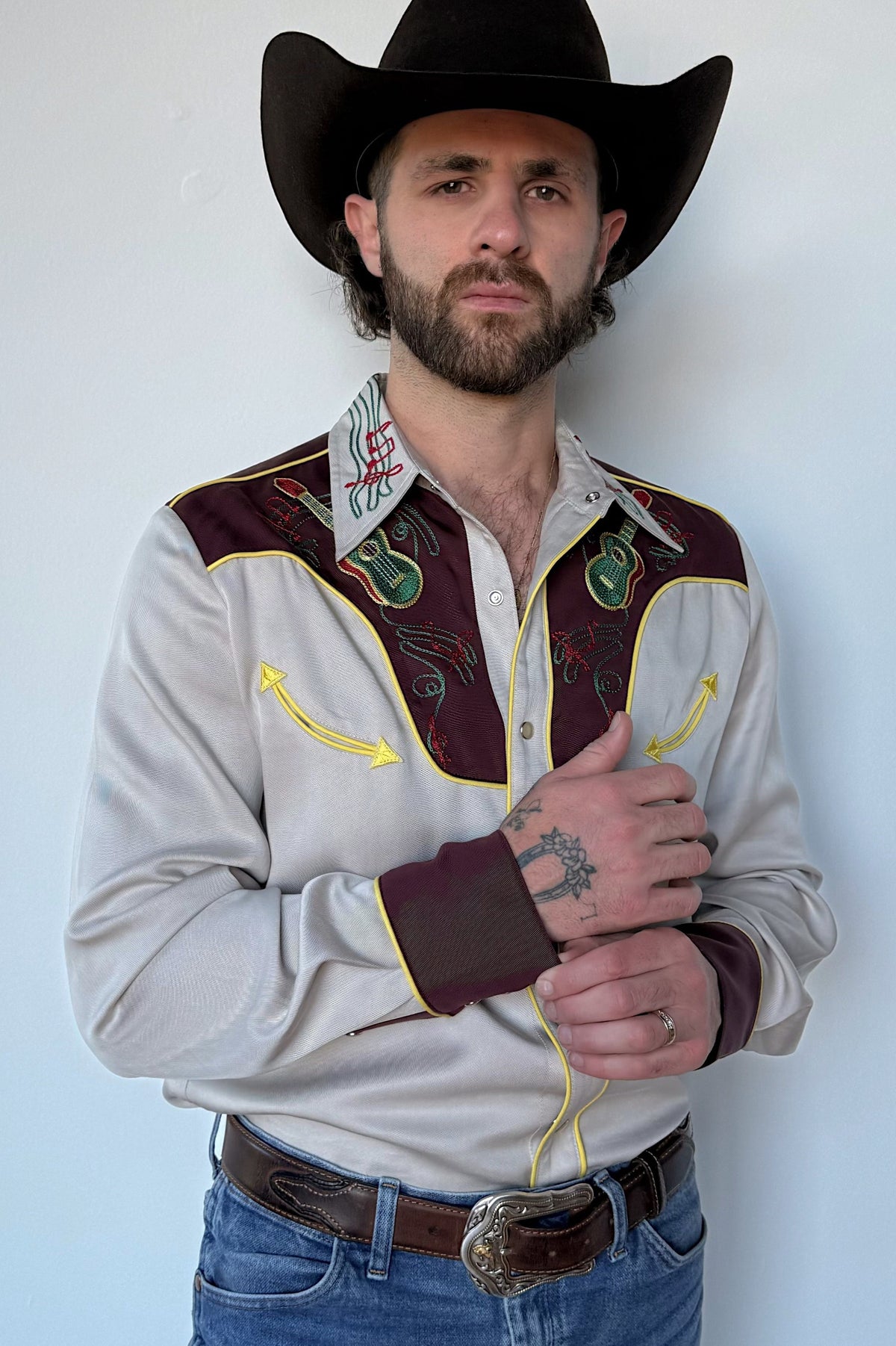 Man in a black cowboy hat wearing the H Bar C Cowboy Bob shirt in cream with maroon yokes, green embroidery, and yellow piping, an early 1950s remake.