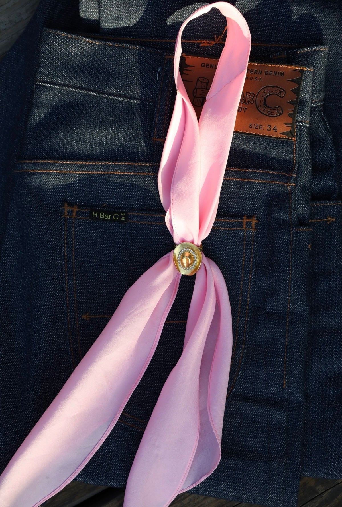 H Bar C rhinestone cowboy hat scarf slide styled with a pink scarf on indigo jeans.