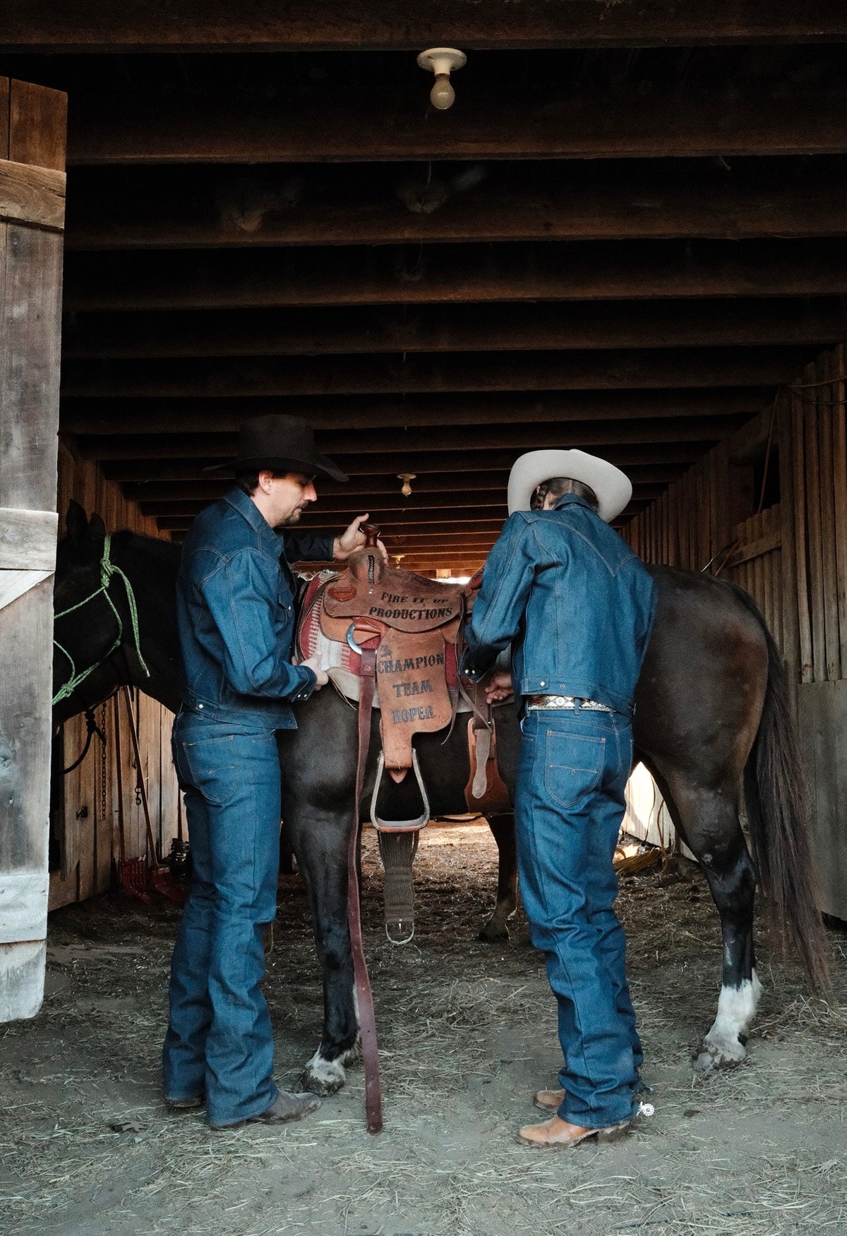 Two cowboys in a barn with a saddled horse, wearing H Bar C indigo denim boot cut flare jeans and denim jackets.