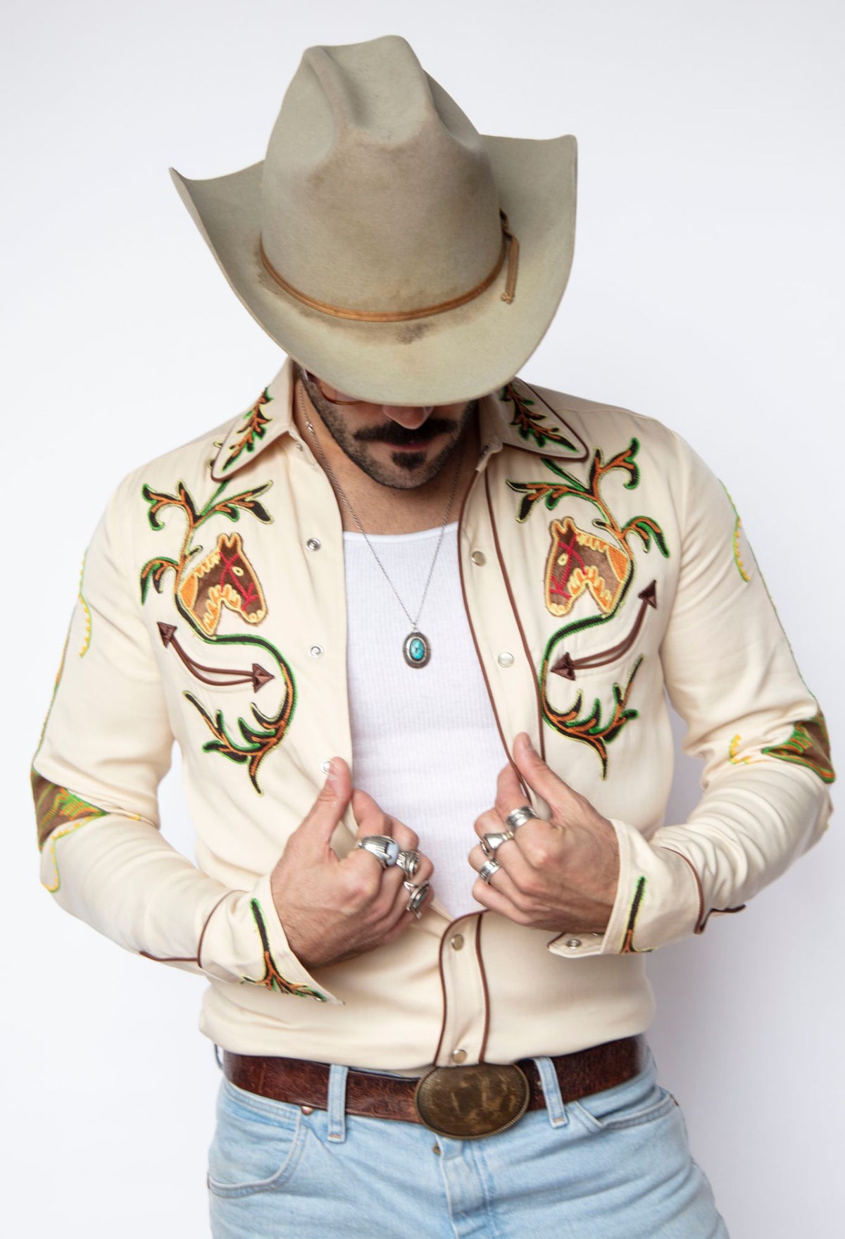 H Bar C Calabasas off-white western shirt with embroidered horse heads, cactus, and floral vines, worn open over a white tank.