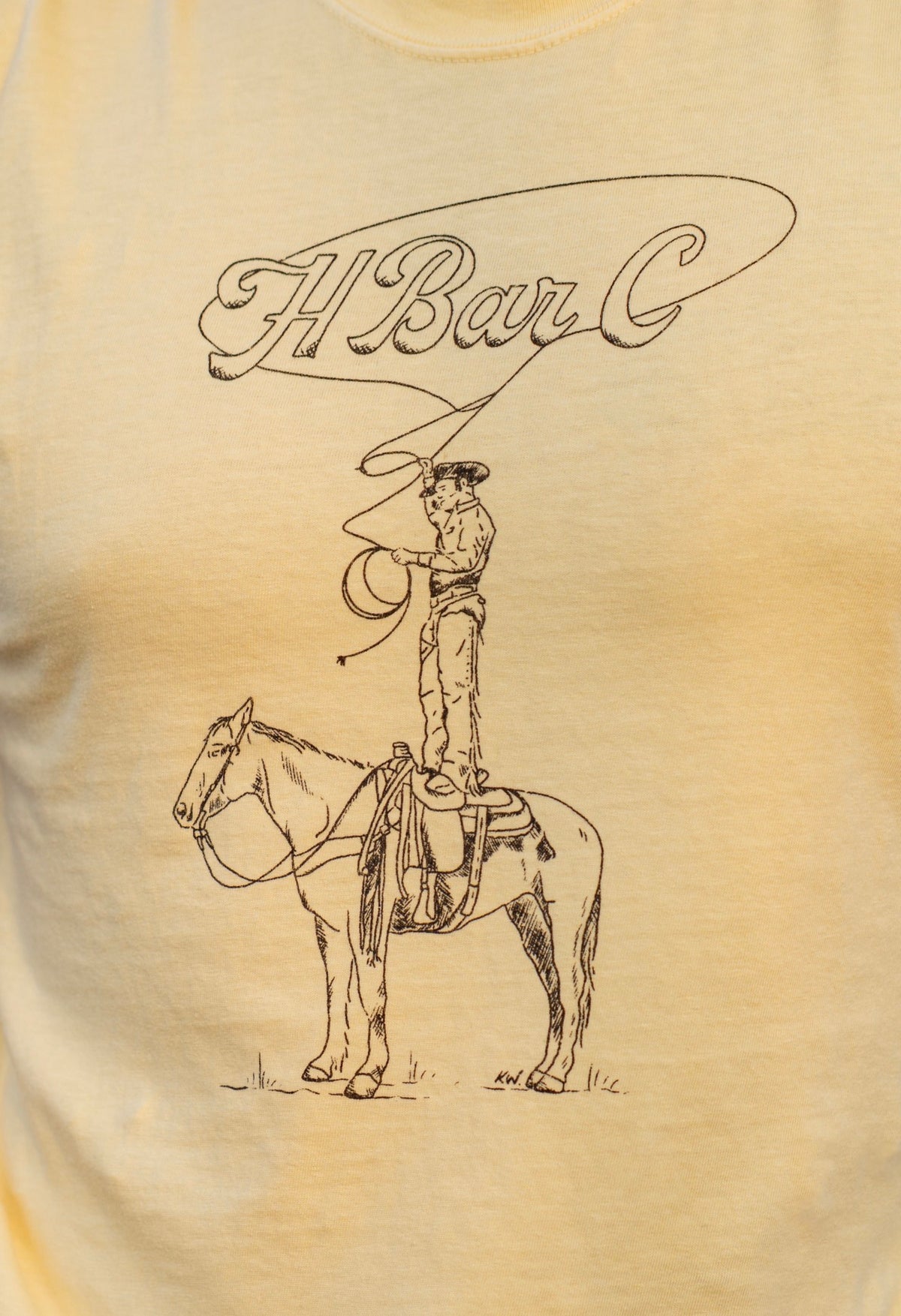 Detail of the hand-drawn Tall Saddle graphic and H Bar C script on the yellow tee.