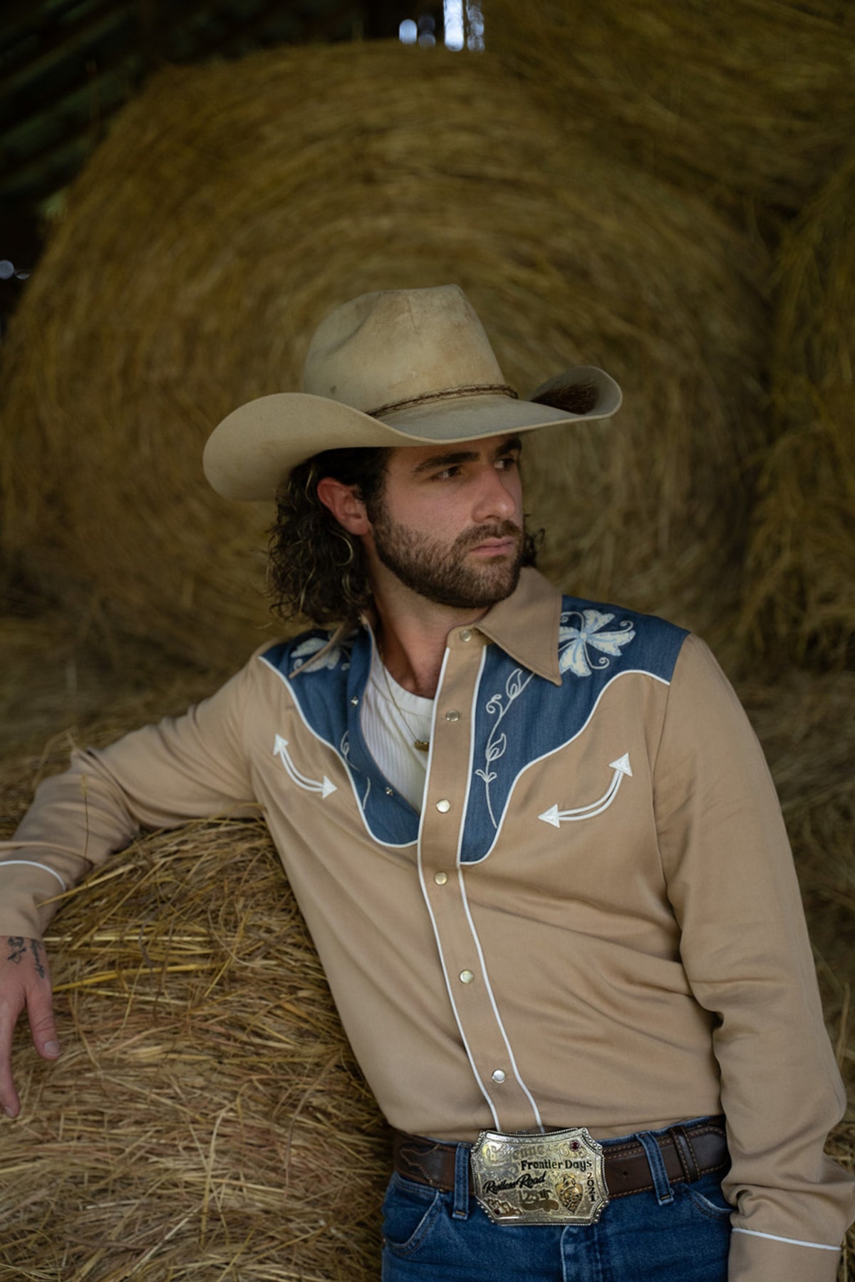 Man in a cowboy hat sitting against hay bales wearing the H Bar C Telluride tan western shirt with embroidered denim yoke.
