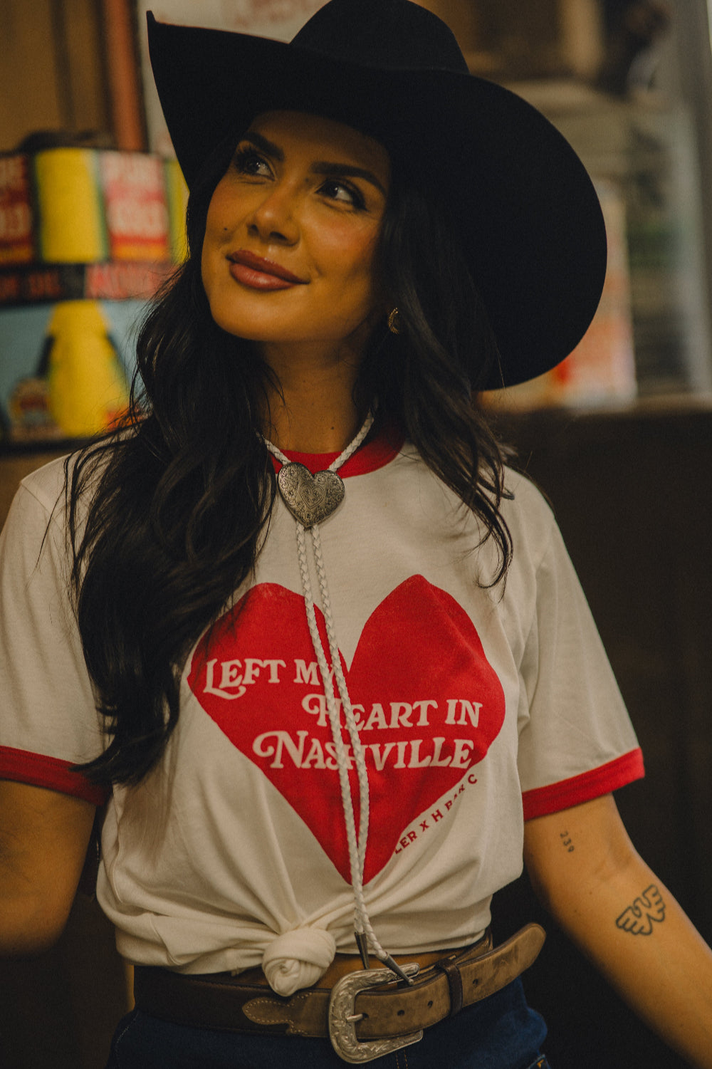 Woman in a black cowboy hat wearing the H Bar C x Rustler Left My Heart in Nashville ringer tee with a red heart graphic.