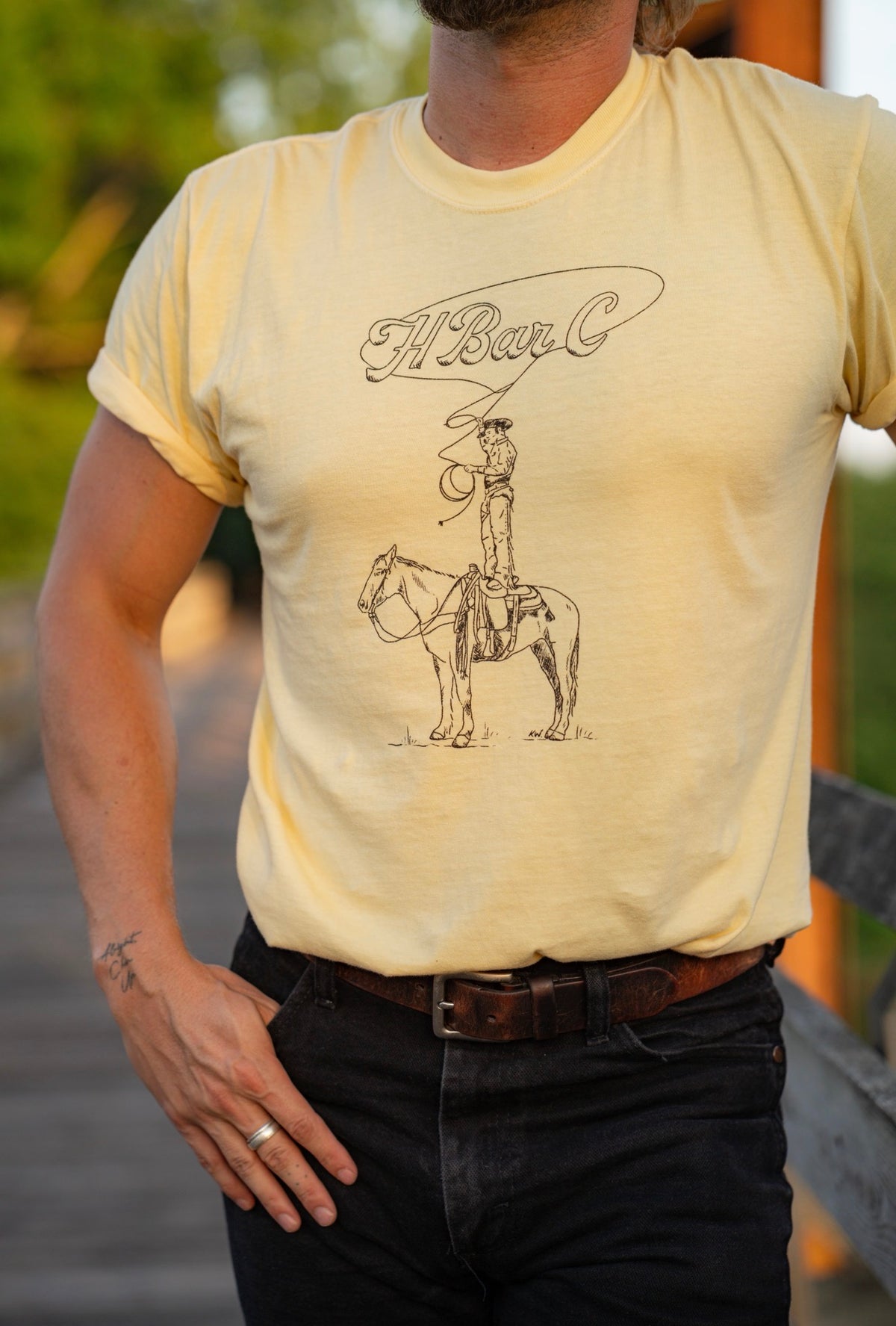 Close-up of the H Bar C Tall Saddle yellow T-shirt with hand-drawn cowboy standing in the saddle.