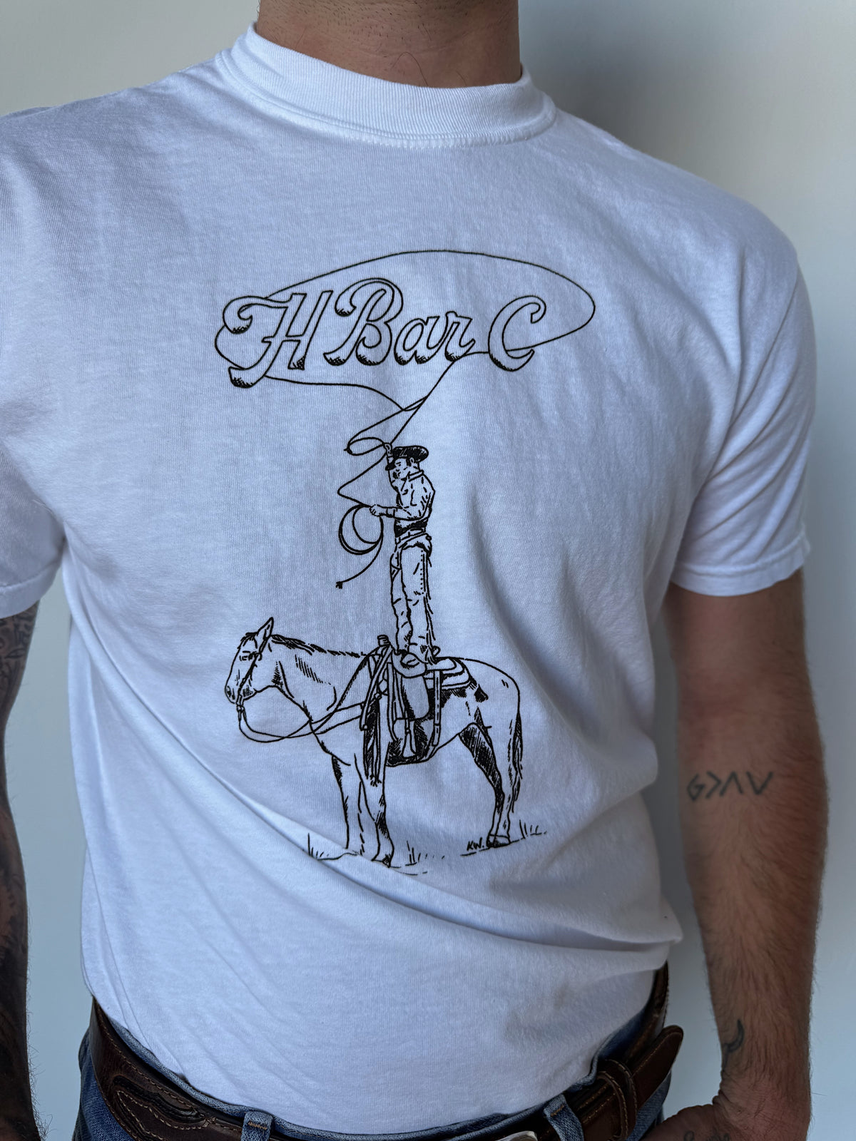 Close-up of the hand-drawn Tall Saddle cowboy graphic and H Bar C script on the white tee.