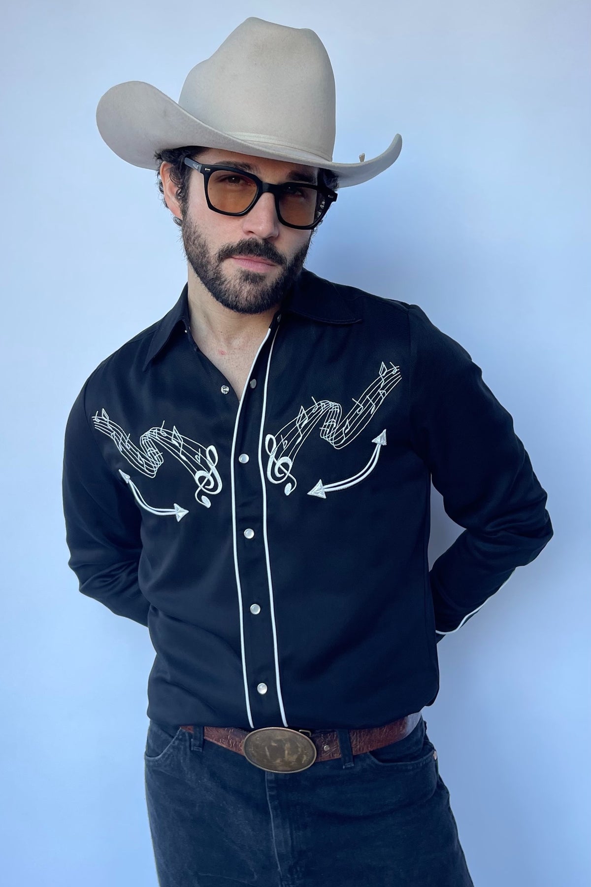 Man in a cowboy hat wearing the H Bar C Nashville shirt in black with white music-inspired embroidery.