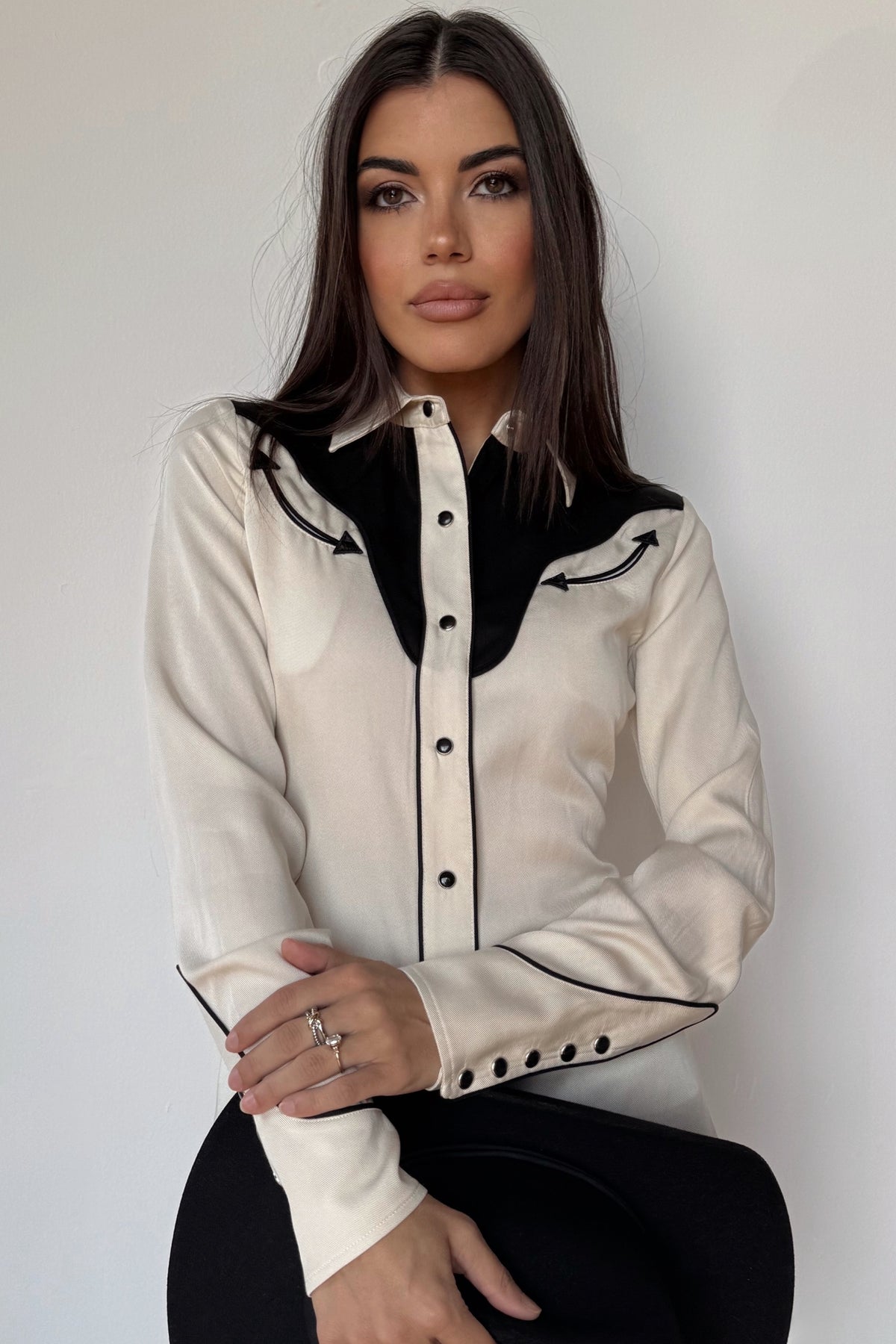 Woman holding a black cowboy hat wearing the H Bar C San Juan women's shirt in off white with black yokes and piping.