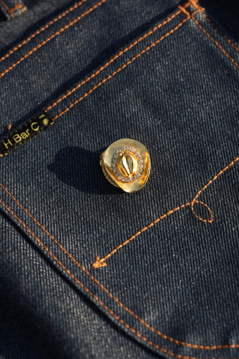 Gold rhinestone cowboy hat scarf slide by H Bar C on an indigo denim pocket.