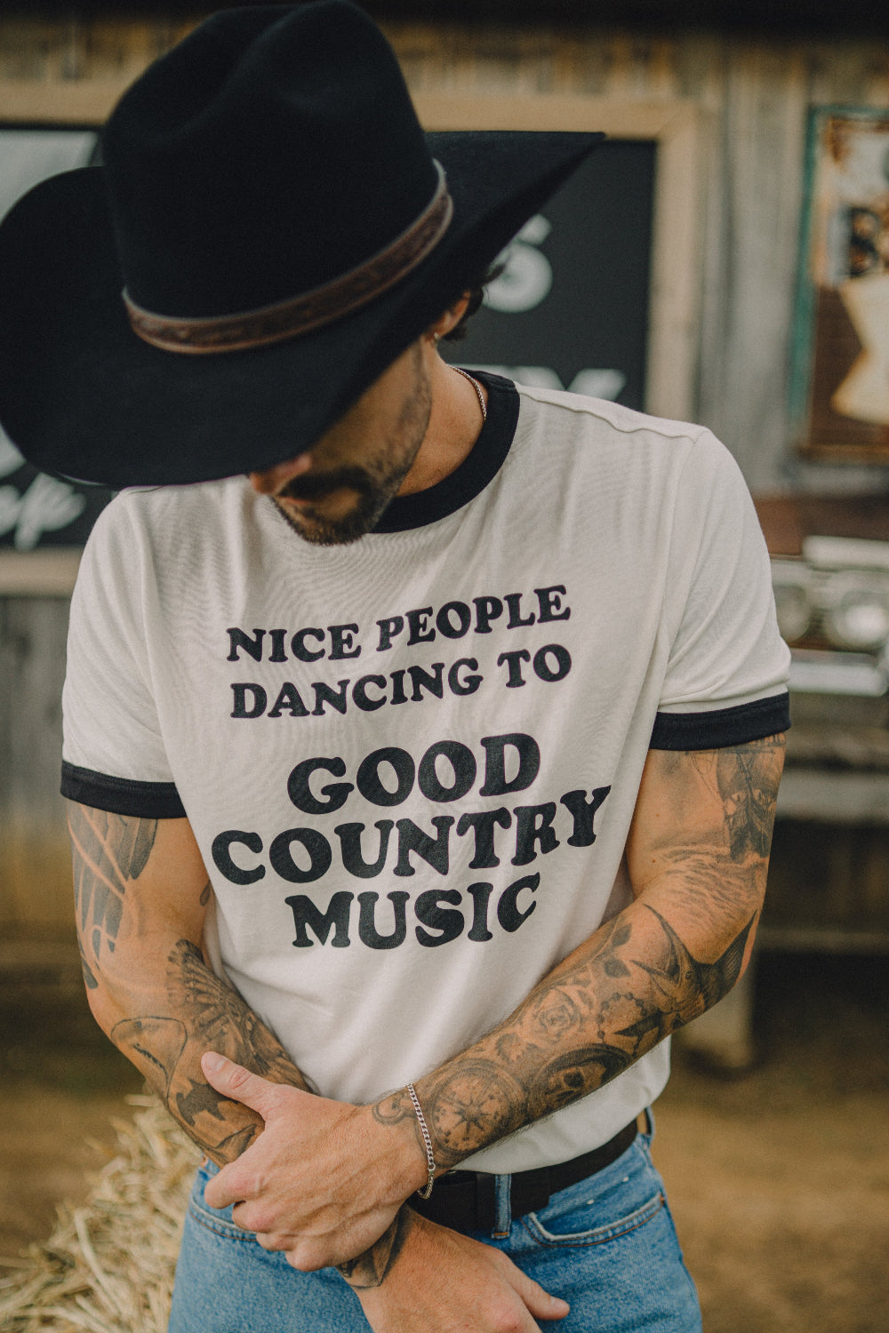 Man in a black cowboy hat wearing the H Bar C x Rustler Nice People Dancing to Good Country Music men's ringer tee.