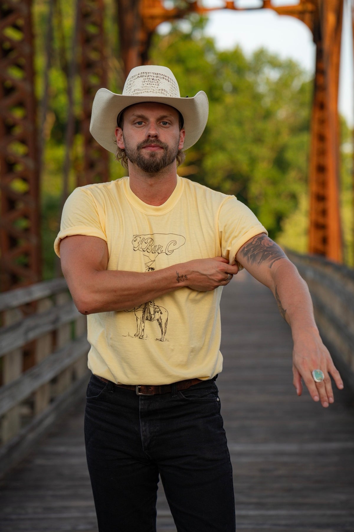 Man wearing the yellow H Bar C Tall Saddle graphic T-shirt with black jeans outdoors.