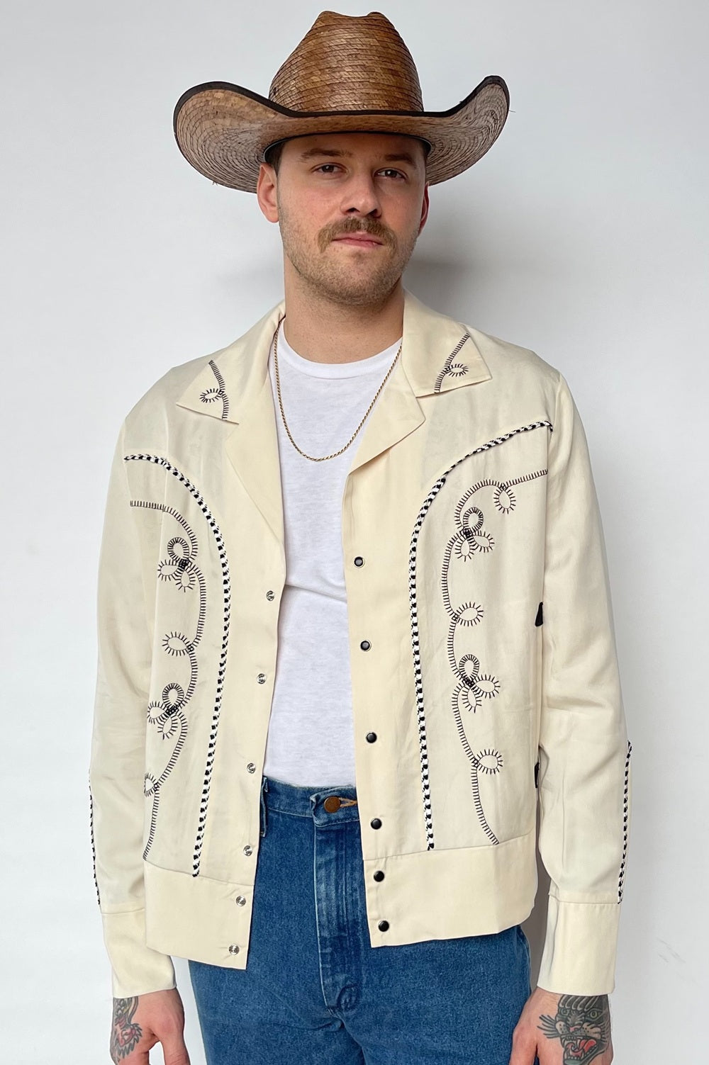 Man in a brown cowboy hat wearing the H Bar C Bolero men's jacket in off-white with brown chain stitch embroidery.