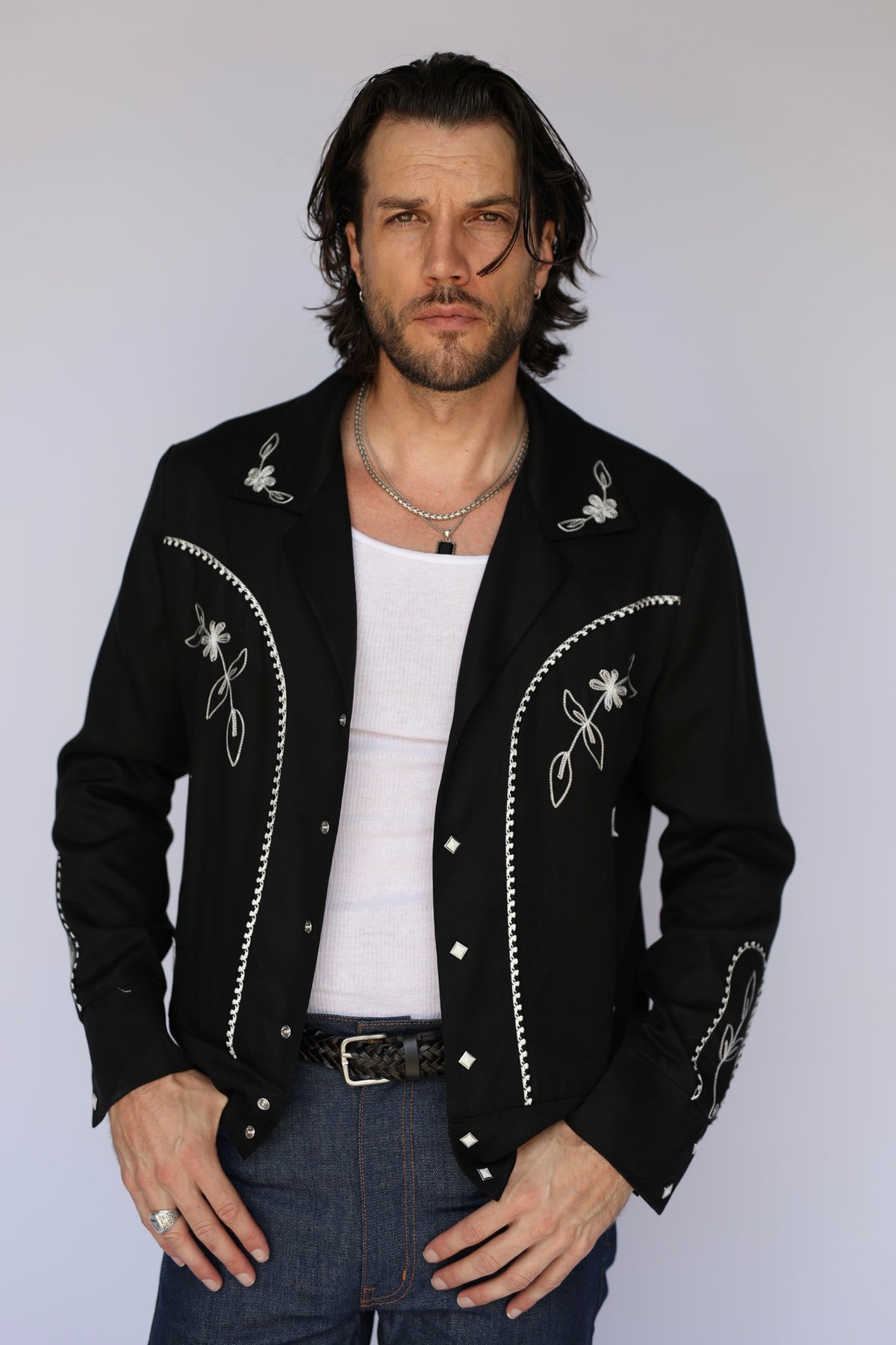 Man wearing the H Bar C Bolero Nogales men's jacket in black and white, a hip-length bolero with floral chain stitch and studs.