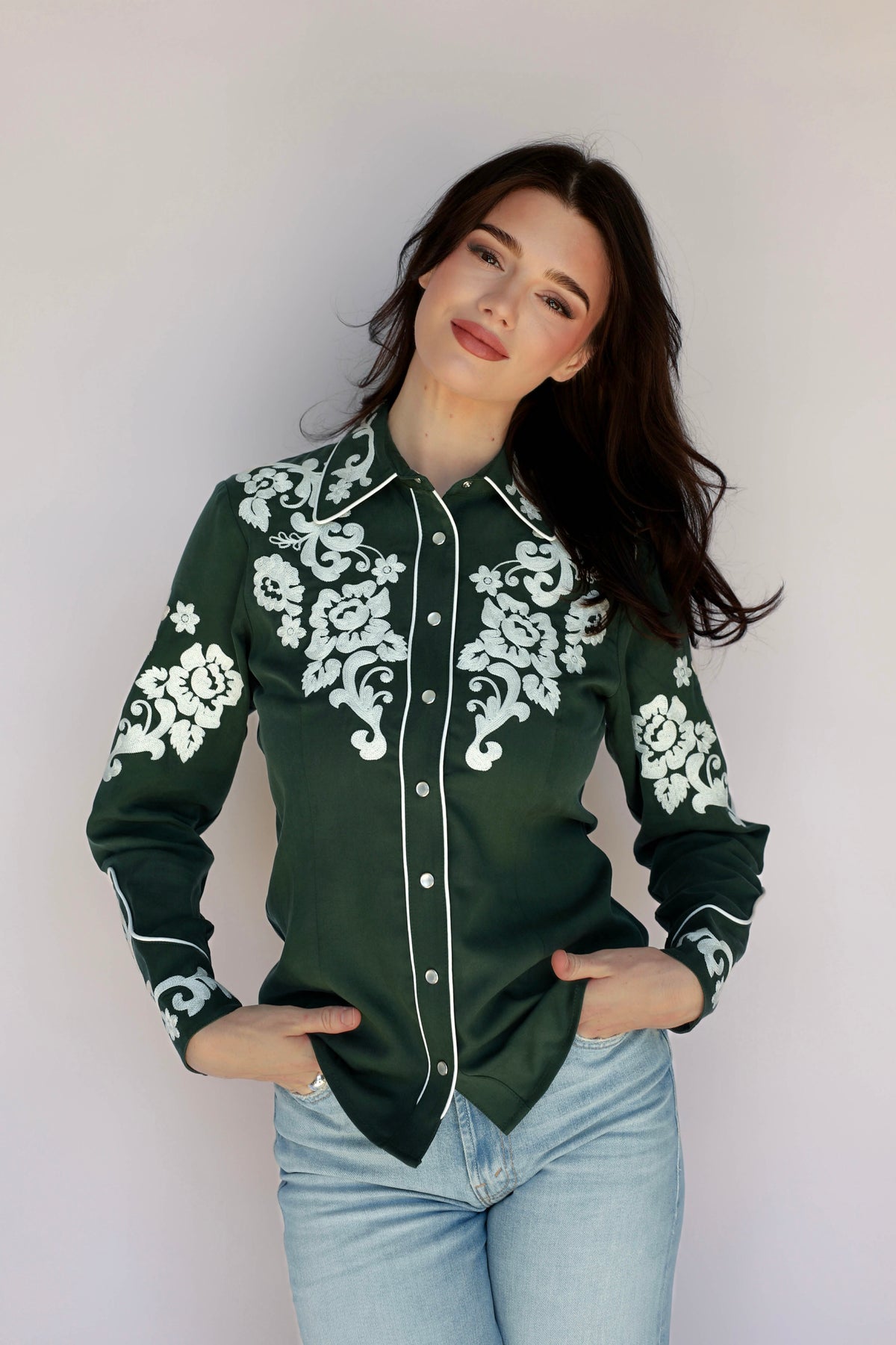 Woman wearing the H Bar C Fort Worth women's shirt in green with white floral embroidery, with light jeans.