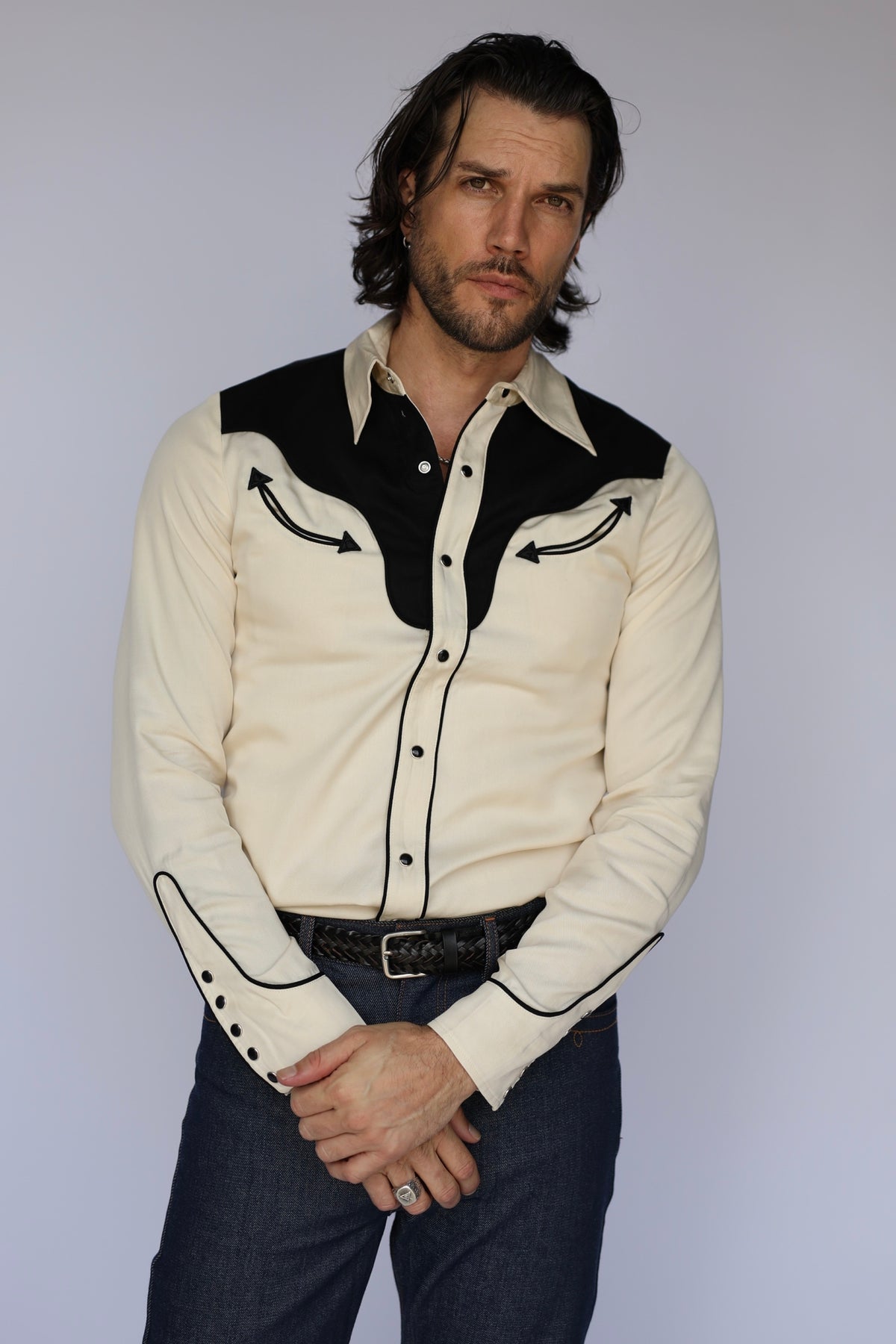 Man wearing the H Bar C San Juan men's shirt in off-white with black yokes, black piping, and arrow smile pockets, with jeans.