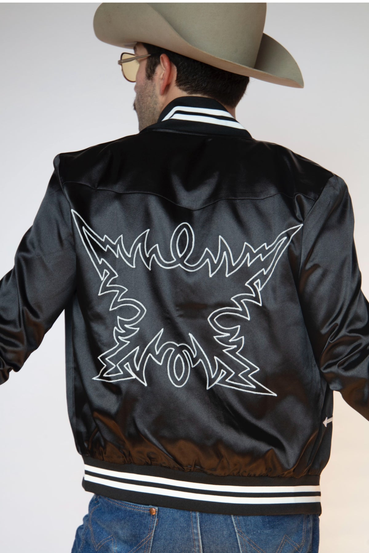 Back view of the H Bar C Odessa black satin tour jacket with white chain stitch back embroidery.