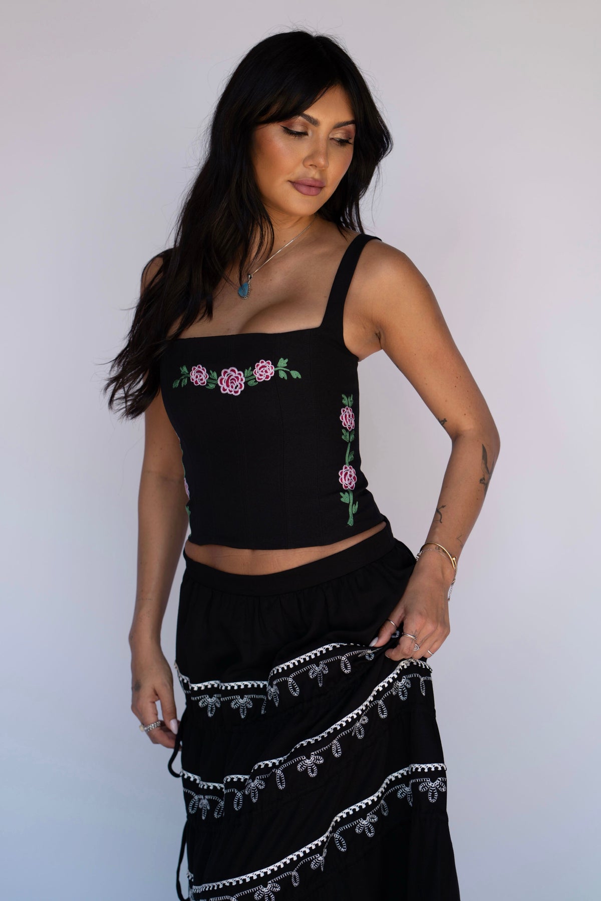 Woman wearing the H Bar C Canterbury corset in black with pink chain stitch roses, paired with a black tiered western skirt.